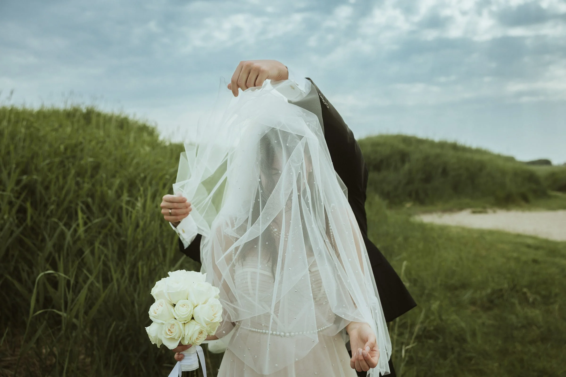 Ein Brautpaar bei einem Spaziergang im Freien, das Brautkleid und Blumenstrauß trägt.