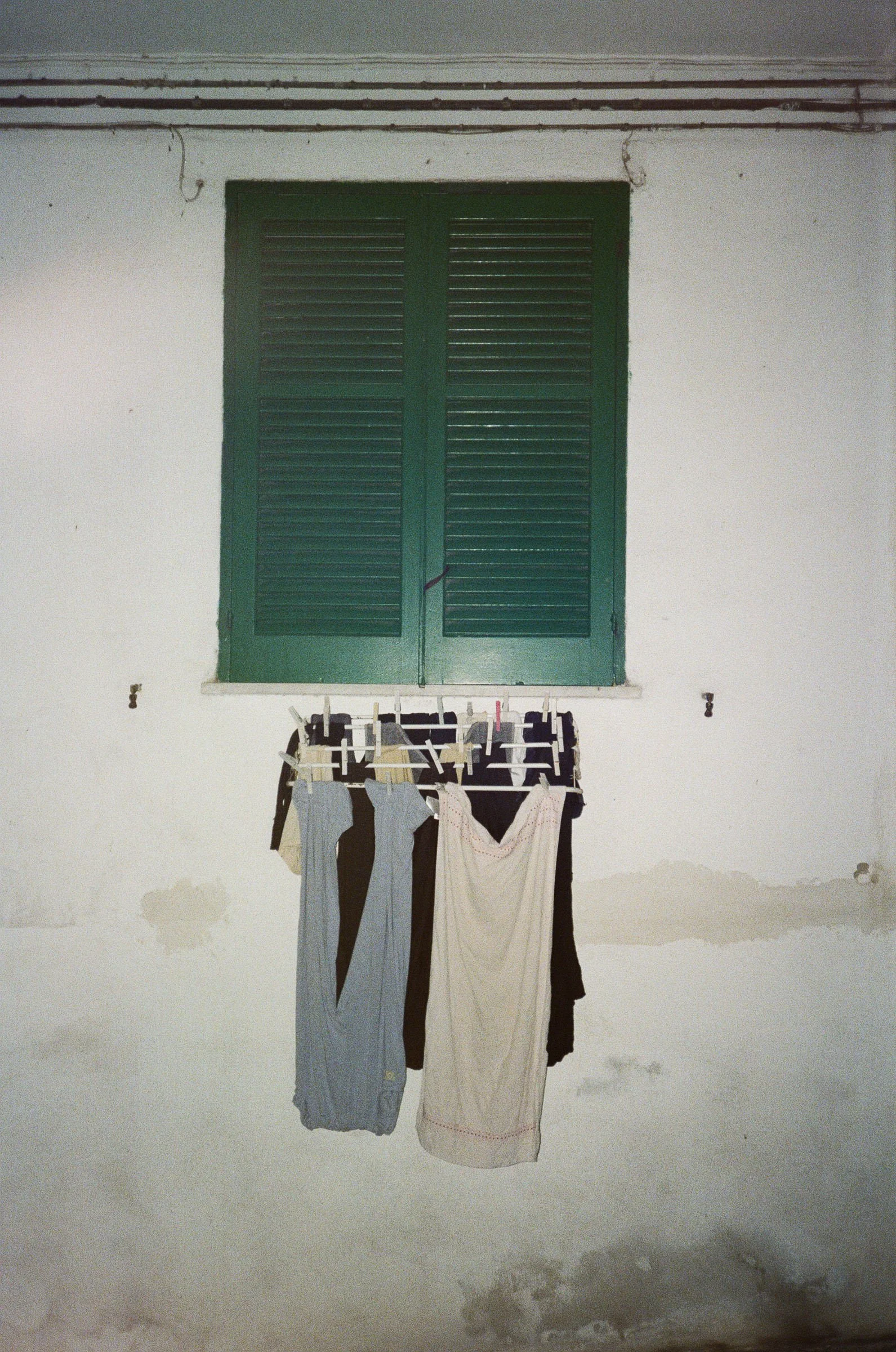 Wäscheleine mit Kleidung im Innenraum vor einer weißen Wand mit einem grünen Fenster.