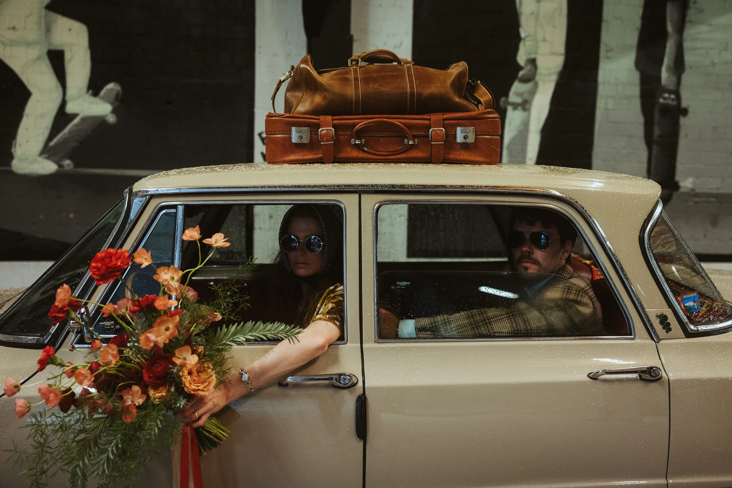 Hochzeitspaar mit großem Blumenstrauß und Vintage Koffern in einem Oldtimer im Skaters Palace Münster