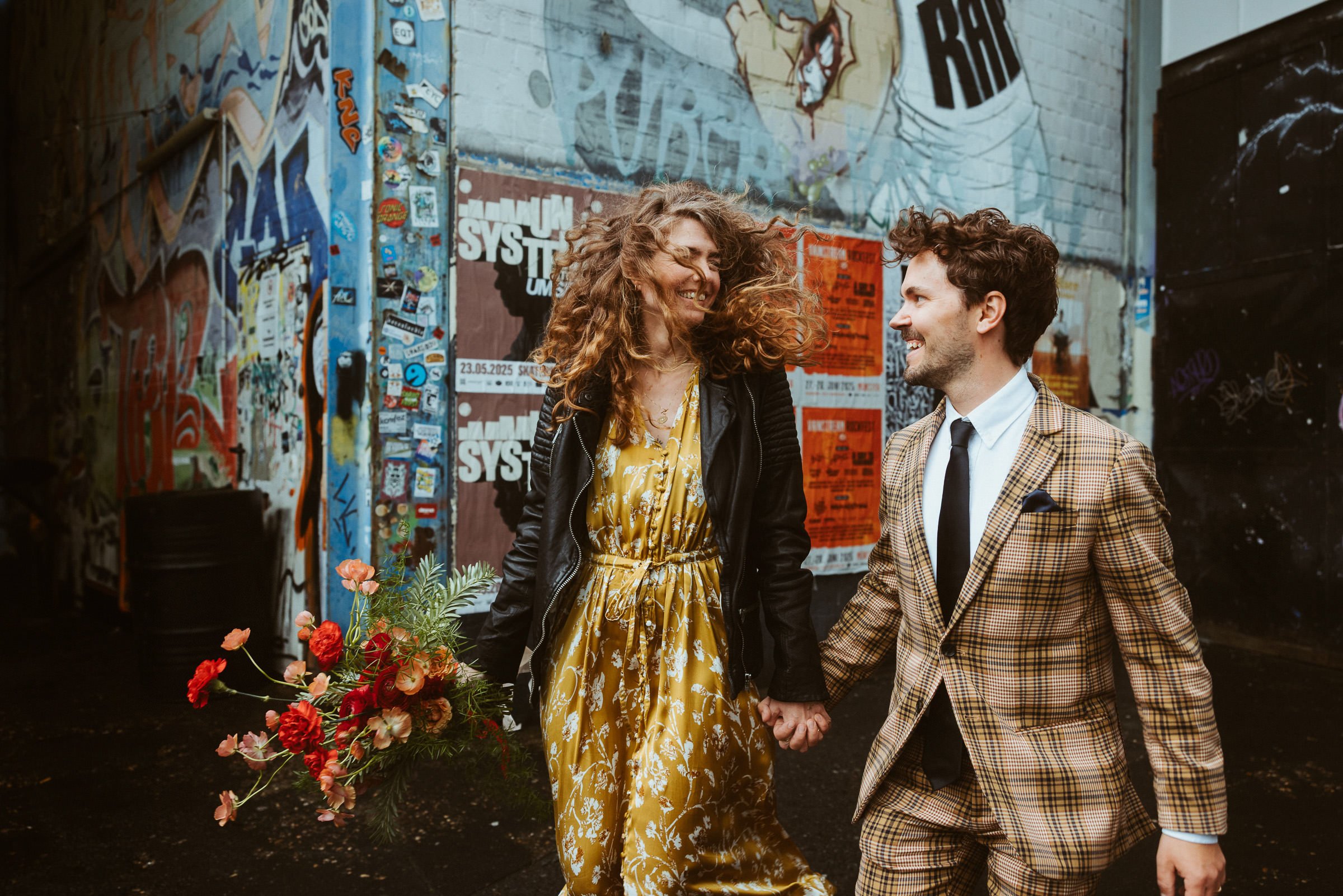 Lachendes Hochzeitspaar läuft Hand in Hand vor Graffiti im Skaters Palace Münster