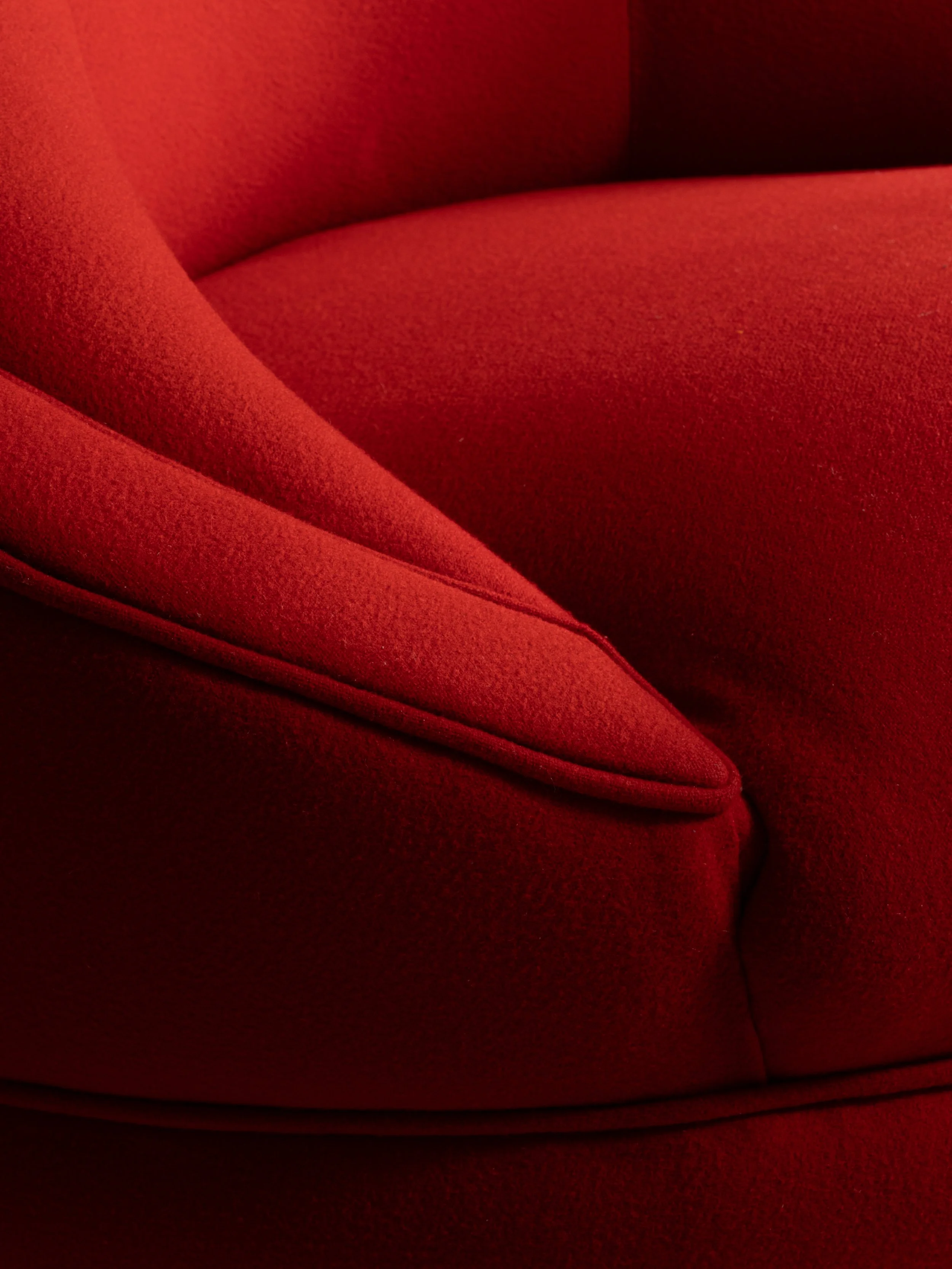 Close-up of a red fabric upholstered chair with curved armrest and seam details.