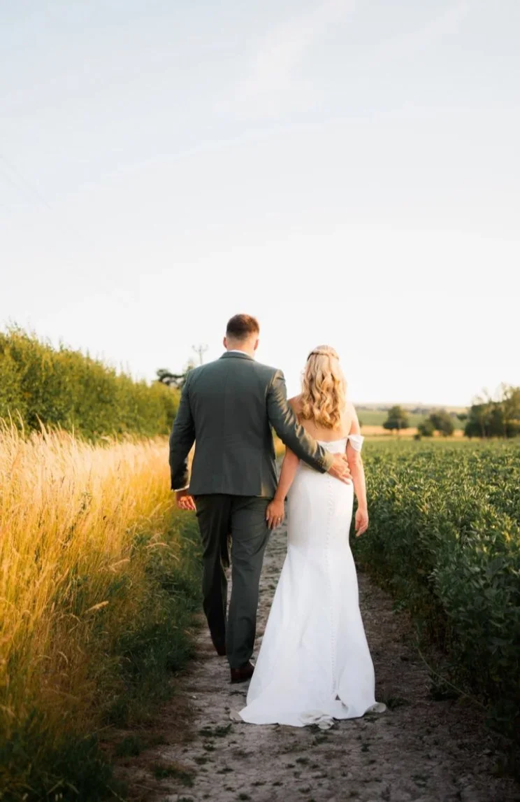 Bride and groom walking through a field at golden hour by Alex Gell Photography.
