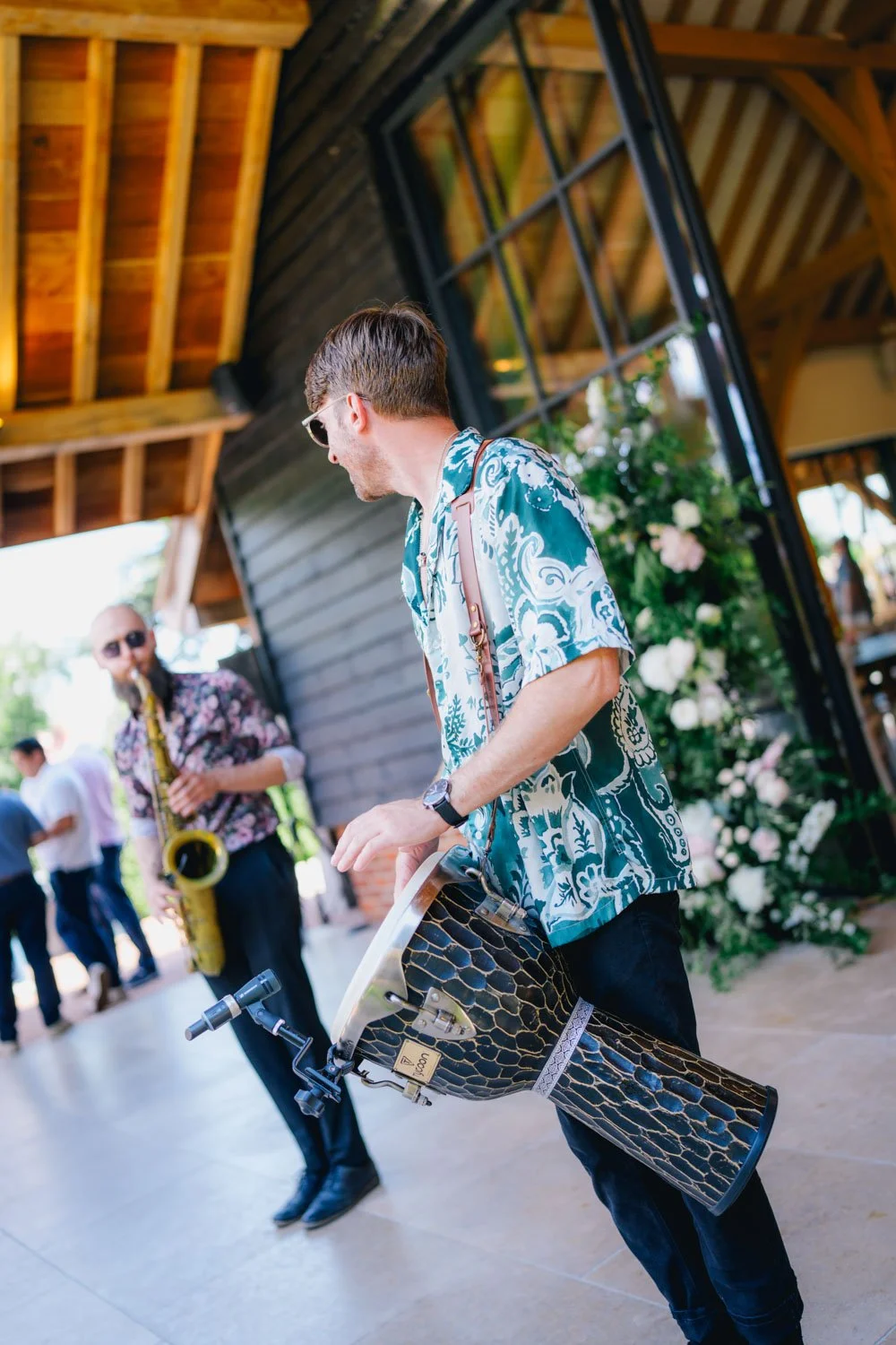 Young man in Hawaiian shirt playing a modern electric trumpet during outdoor event with other musicians.
