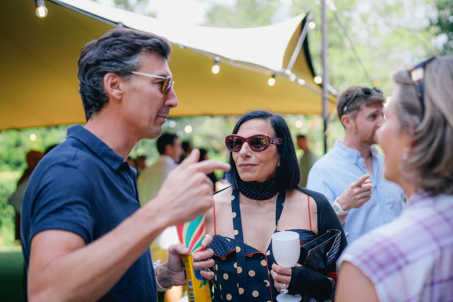 People socializing outdoors at a gathering with string lights and a yellow canopy