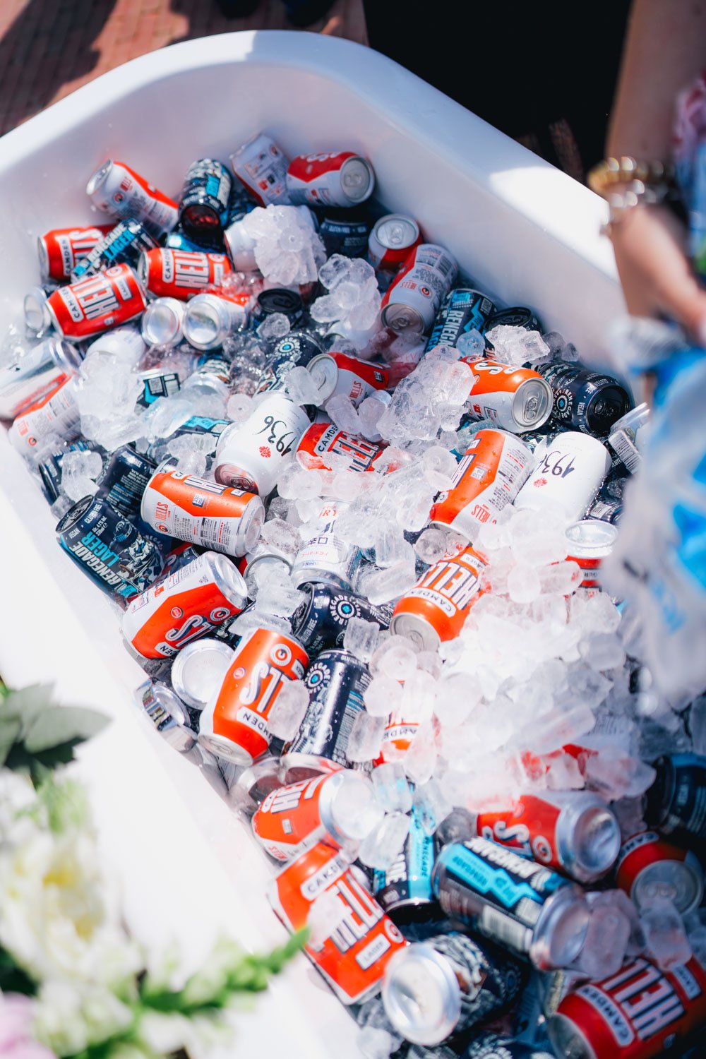 A white ice chest filled with ice and cans of soda, including orange and black cans of Surge and blue cans of Coca-Cola.