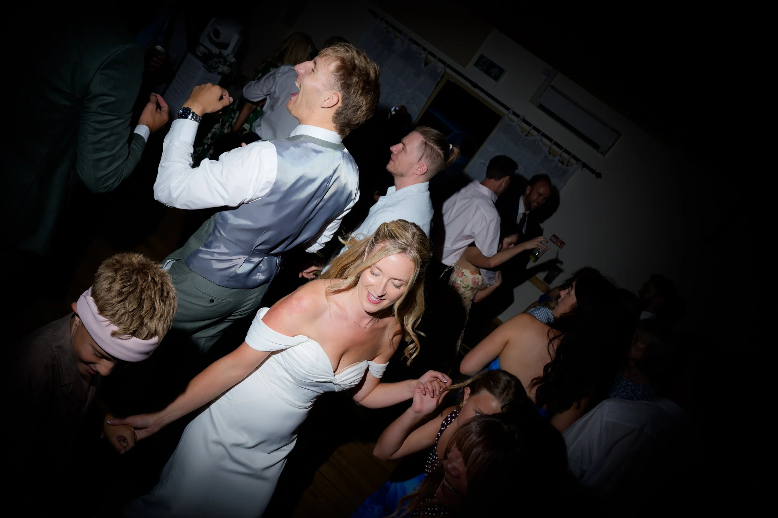 People dancing and socializing at a lively party or celebration in a dimly lit room.