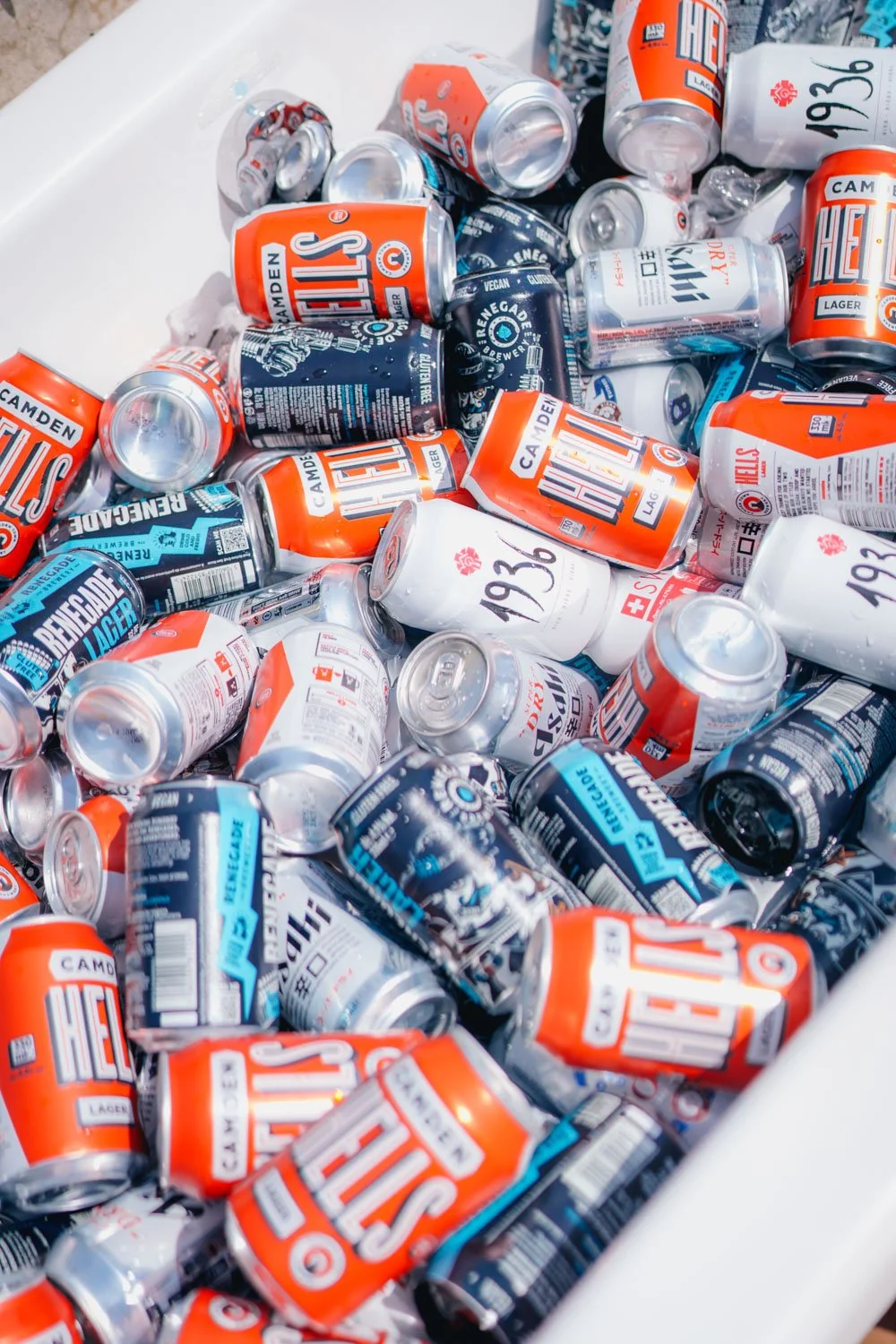 A collection of crushed and whole cans of beer, including brands such as Heineken, Rebellion Lager, and others, inside a white container.
