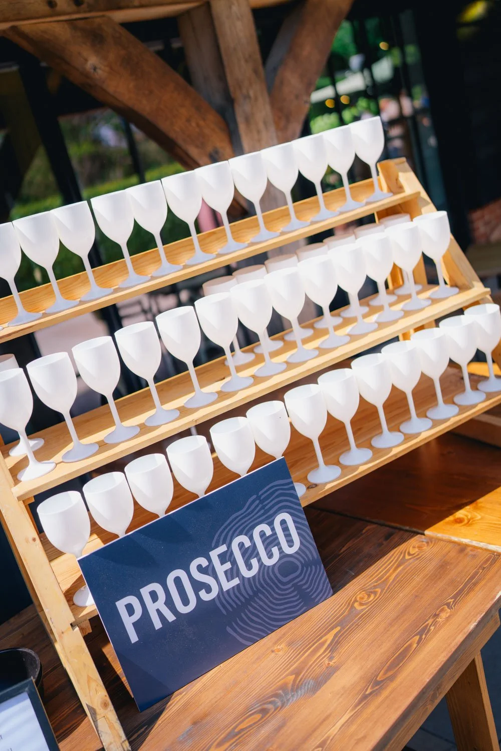 A display of small white Prosecco glasses on wooden shelves with a blue sign that says "Prosecco" in front.