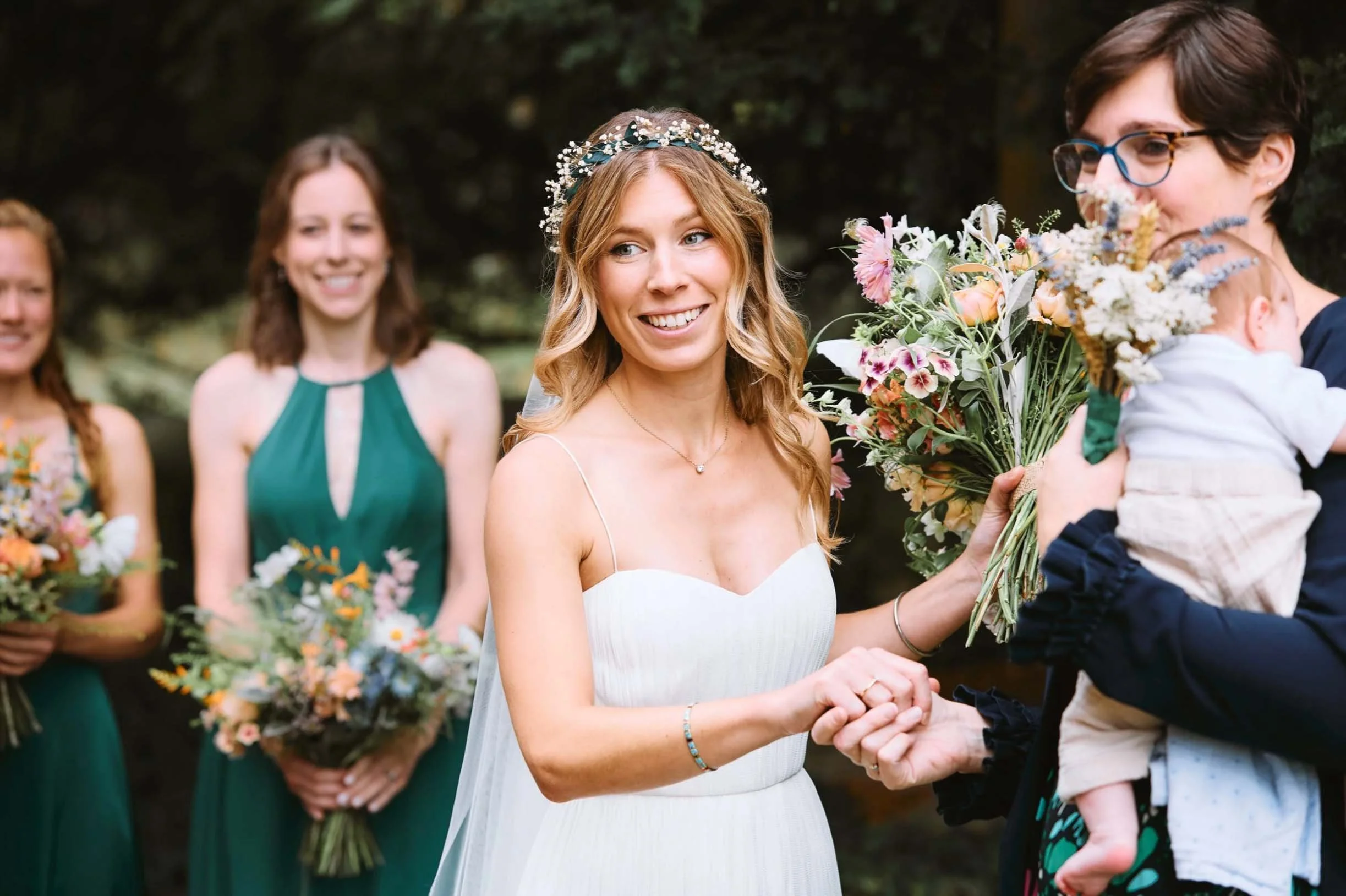Candid moment of a smiling bride wearing a floral crown outdoors with her guests, captured by Alex Gell Photography.