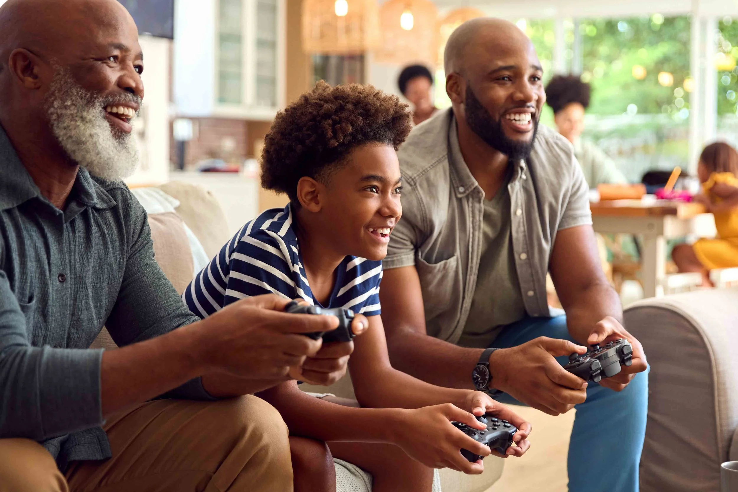 Four people sitting on a couch playing video games, smiling and enjoying their time together in a cozy, well-lit room with large windows.