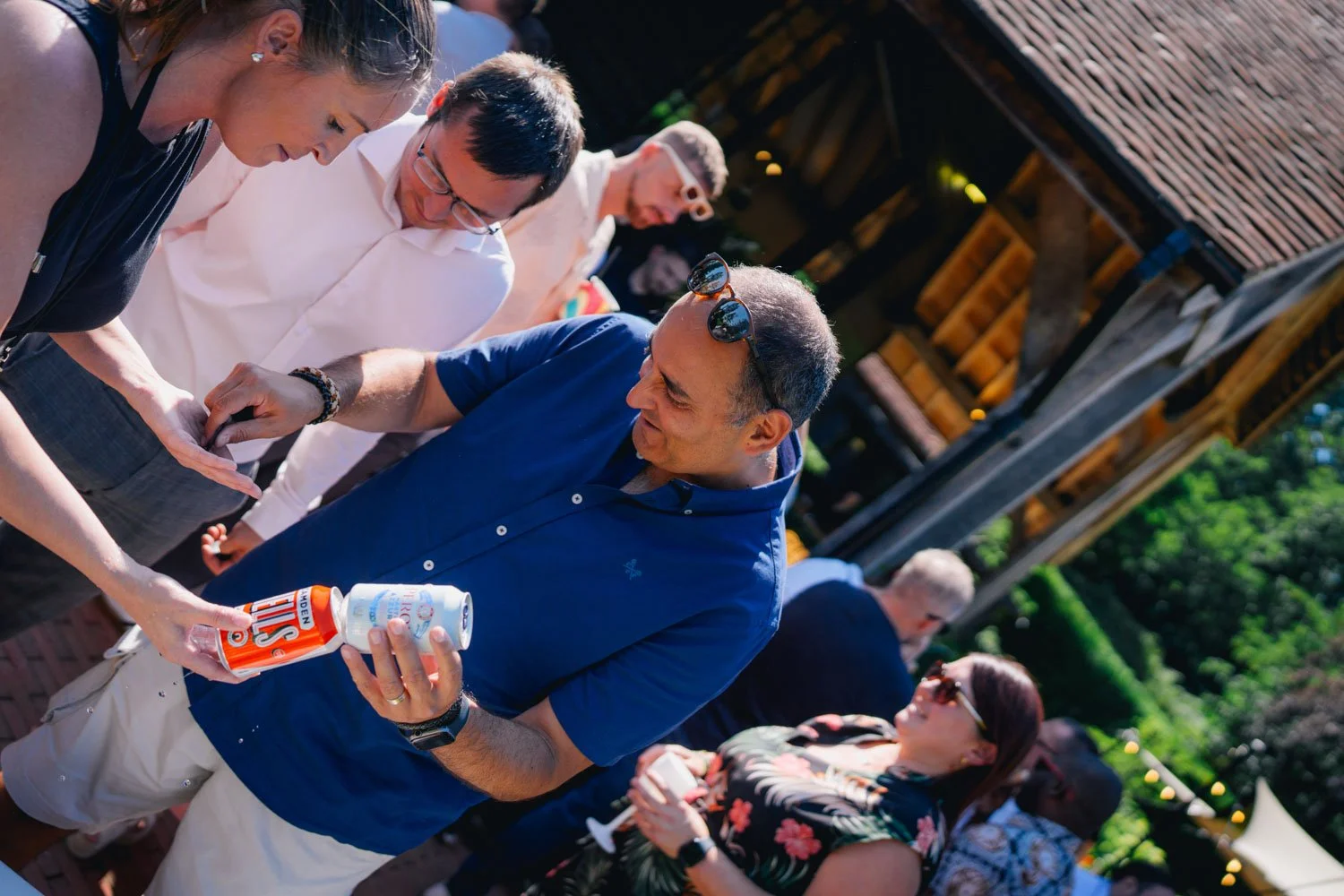 A man in a blue shirt holding a bottle of soda, interacting with a woman in a black top during an outdoor gathering.