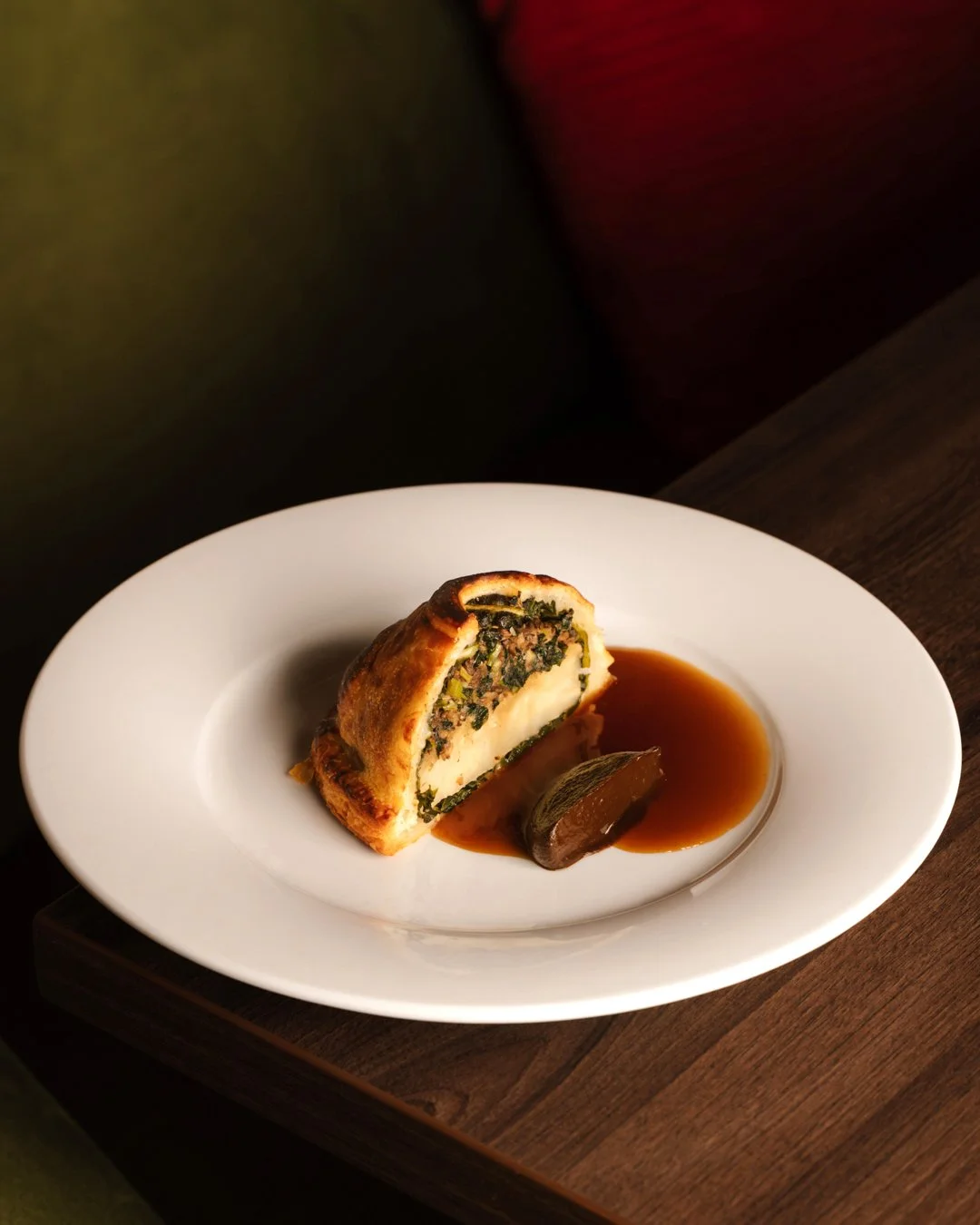 A stuffed pastry with a savory filling, served with brown sauce and a lime wedge on a white plate.