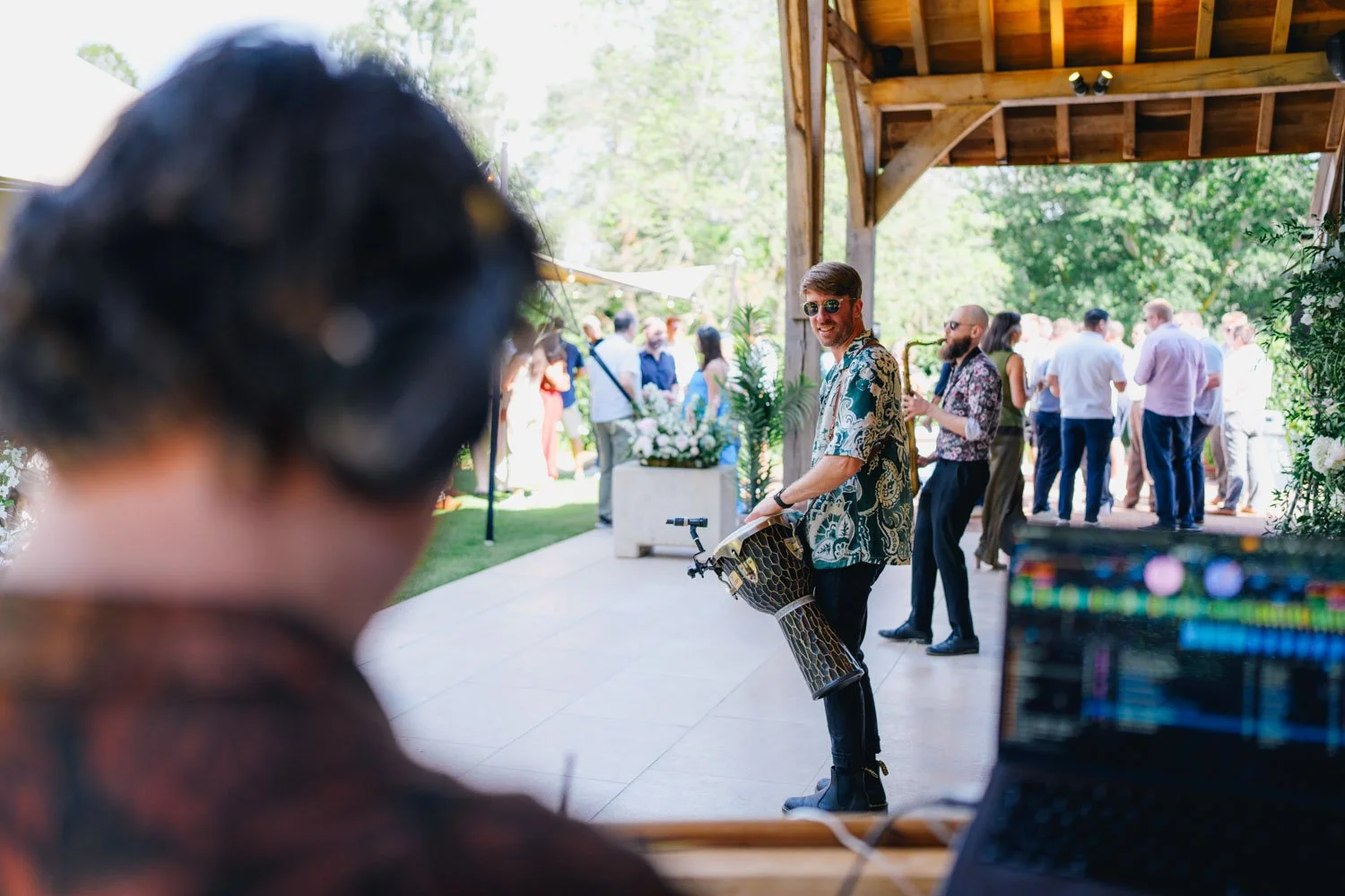 Man with sunglasses holding a drum at outdoor event with people in the background