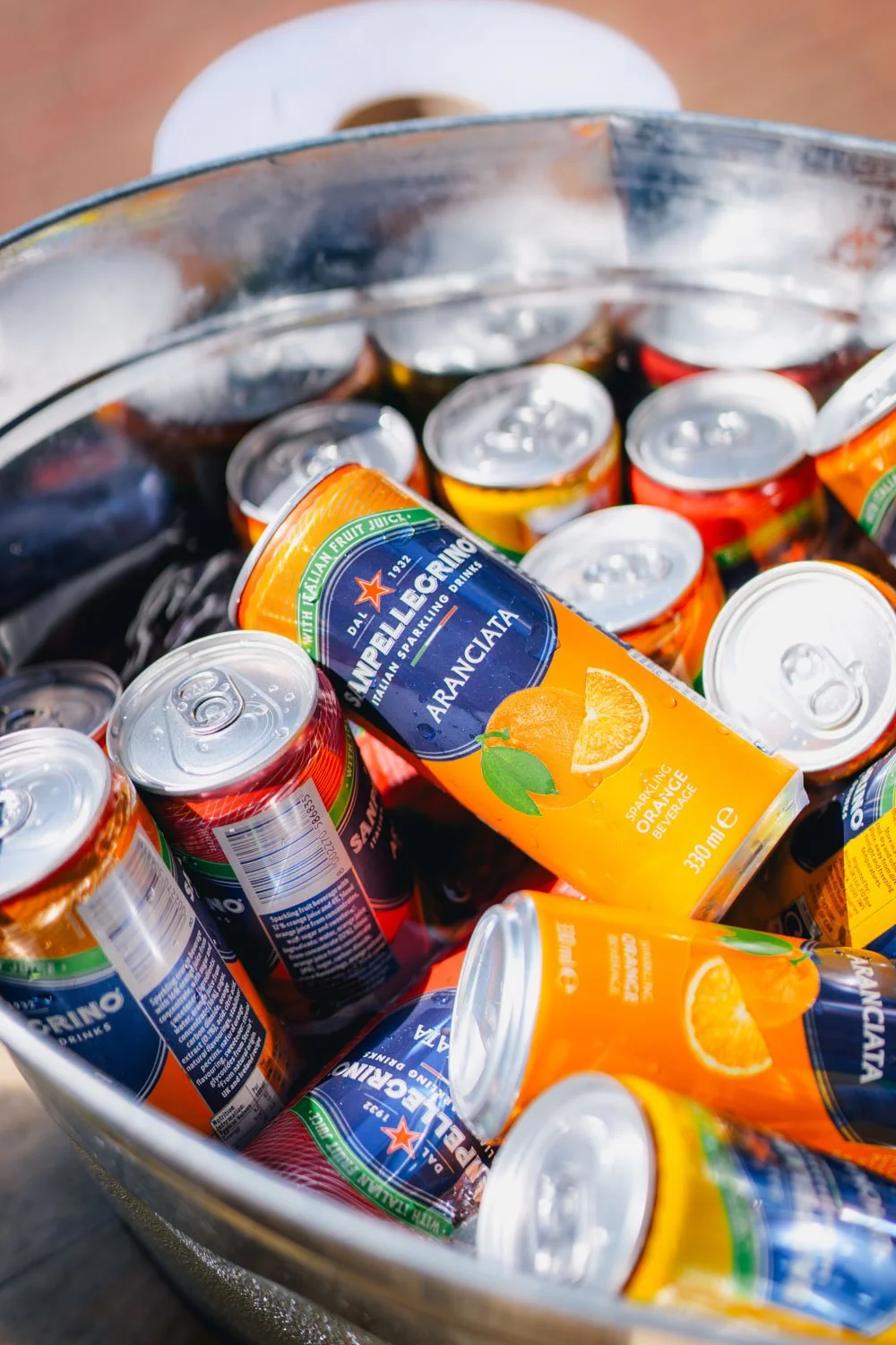 A metal bucket filled with cans of San Pellegrino sparkling orange beverage and other assorted drinks.