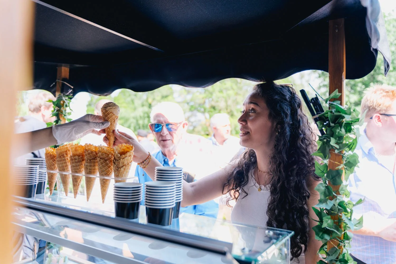 A woman serving ice cream cones at an outdoor event, with multiple people in the background.