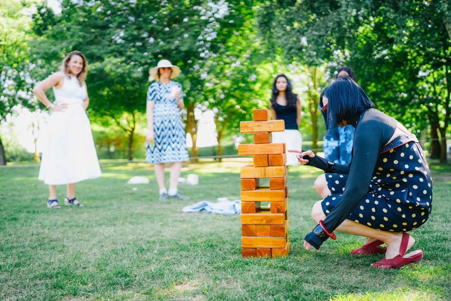 People playing outdoor giant Jenga game in a park with trees in the background.