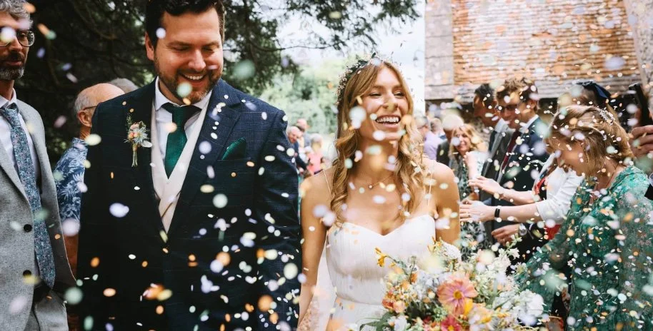 Smiling bride and groom walking through a colorful confetti tunnel thrown by happy wedding guests, natural and candid wedding photography by Alex Gell.