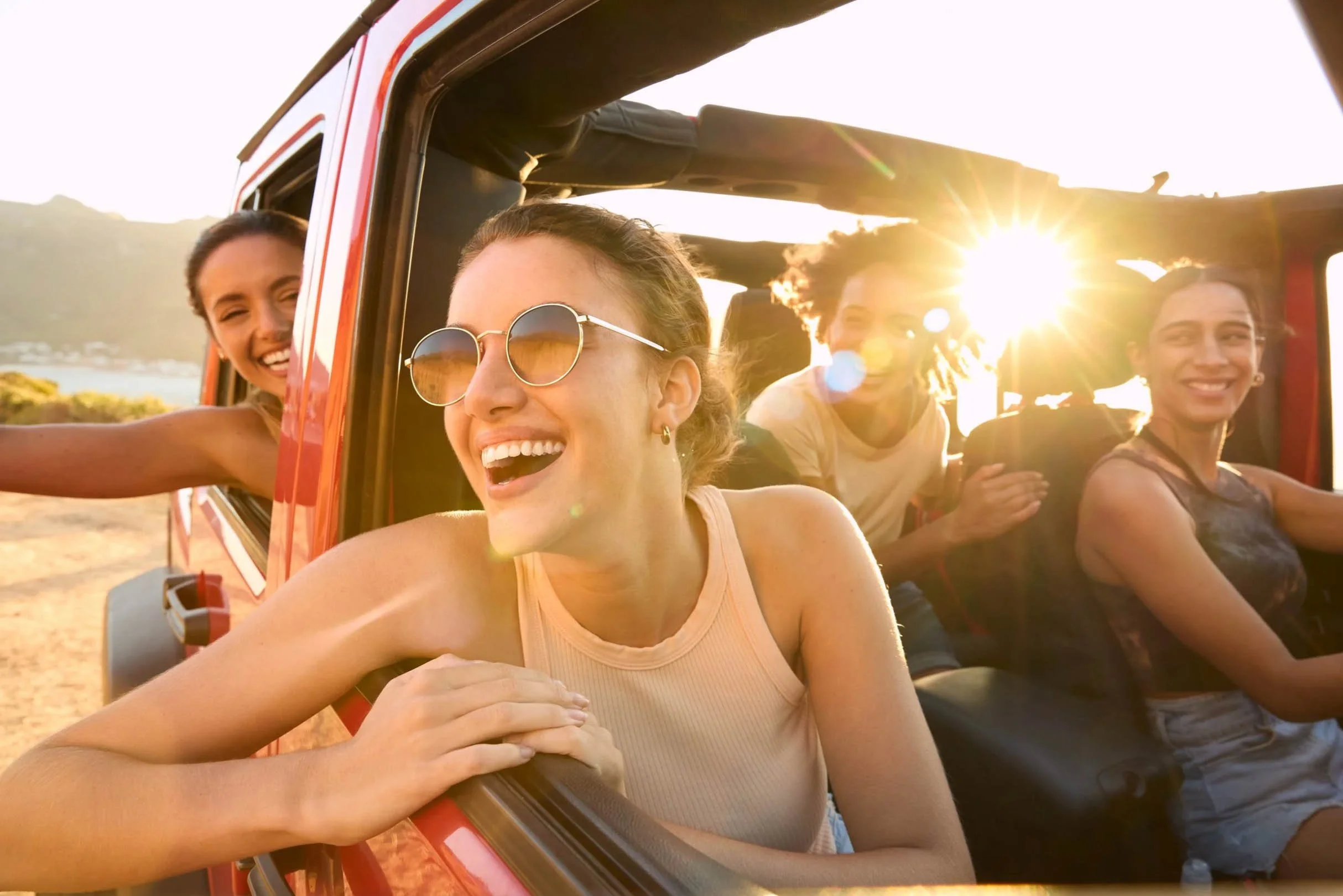 Group of friends laughing in a red convertible jeep at golden hour, outdoor lifestyle brand campaign by Alex Gell Photography.