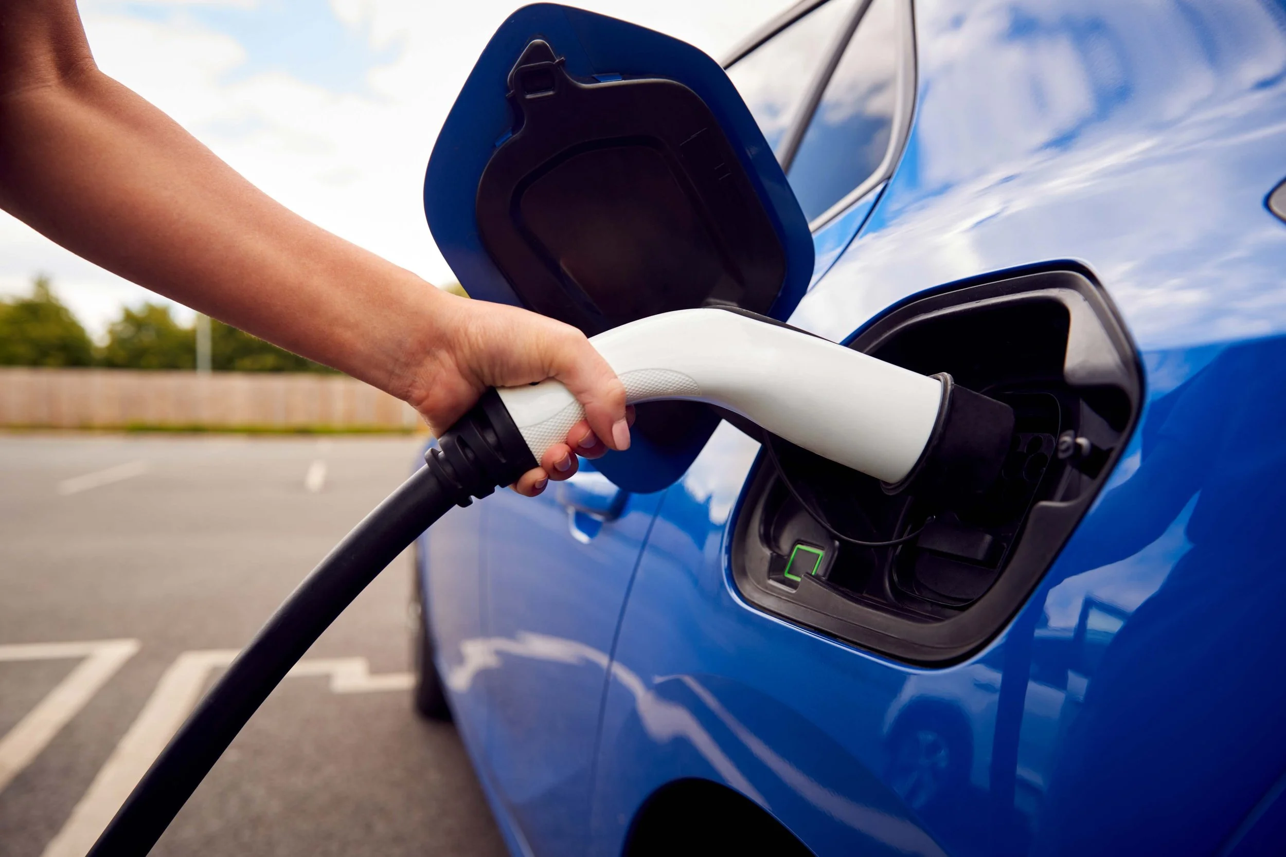 Person plugging in a charging cable to an electric vehicle in an outdoor parking lot.