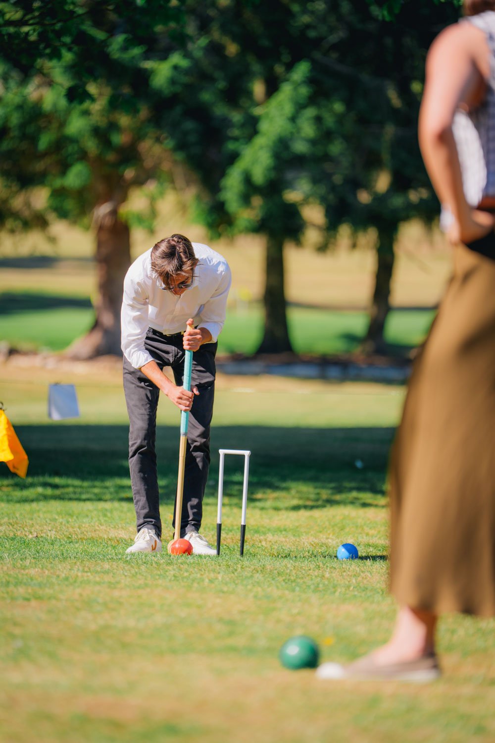 People playing croquet on a sunny day in a park with green trees in the background.
