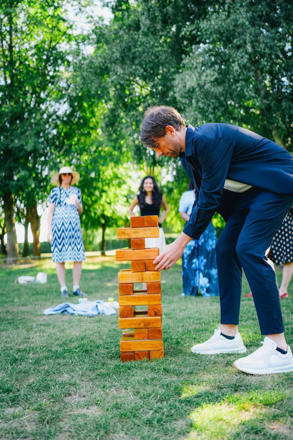 A man playing giant Jenga outdoors with a group of women in a park on a sunny day.
