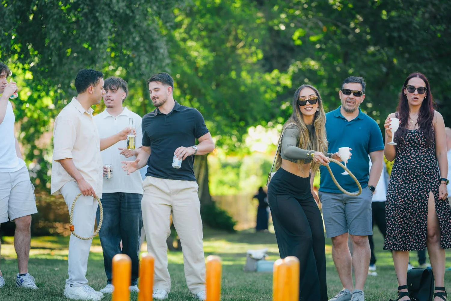 Group of people outdoors playing ring toss and socializing with drinks.