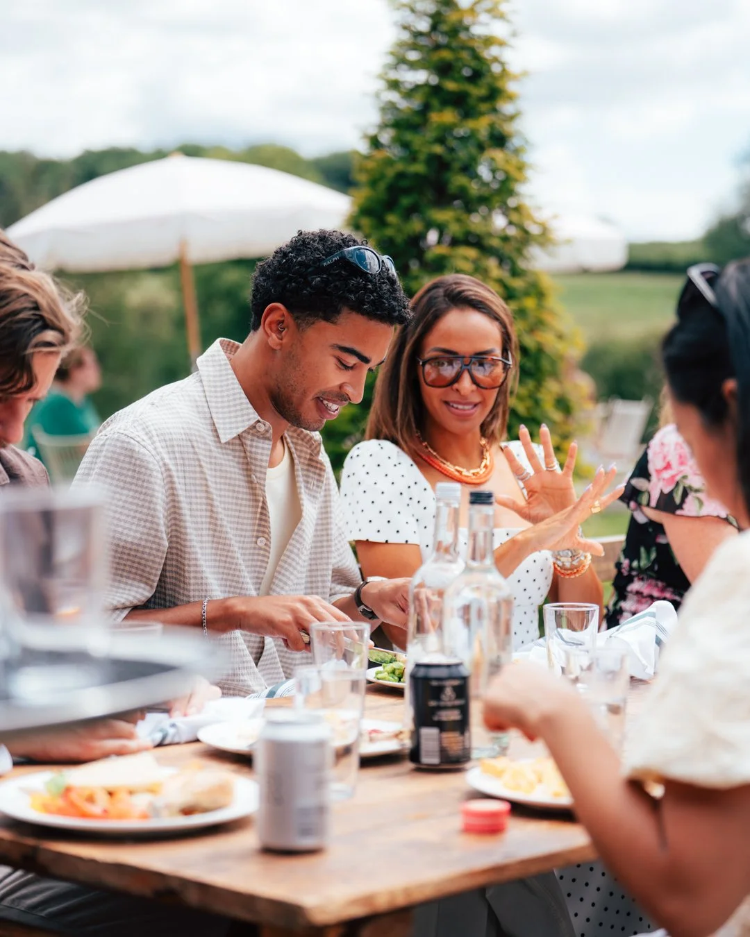 People sitting at an outdoor dinner table, enjoying a meal and conversation on a sunny day.