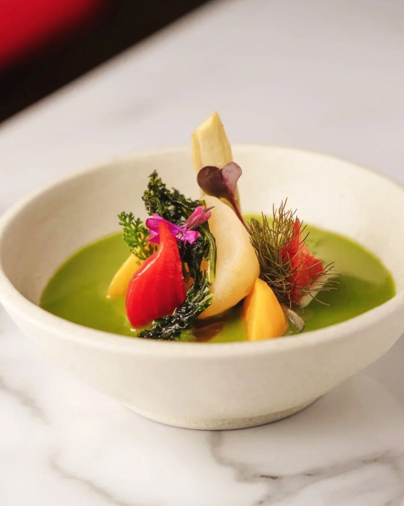 Elegant fine dining dish featuring a bright green purée and colorful vegetable garnishes in a white bowl, London food photography by Alex Gell.