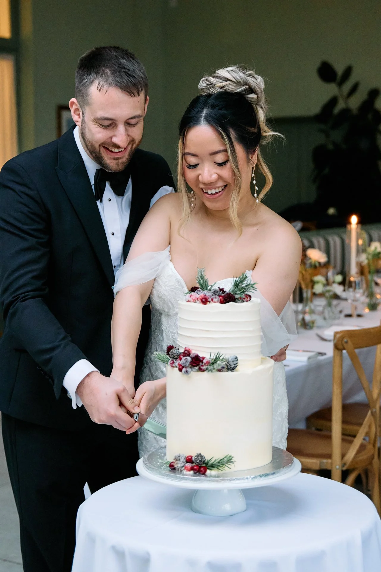 A bride and groom in wedding attire cutting a wedding cake together at their wedding reception.