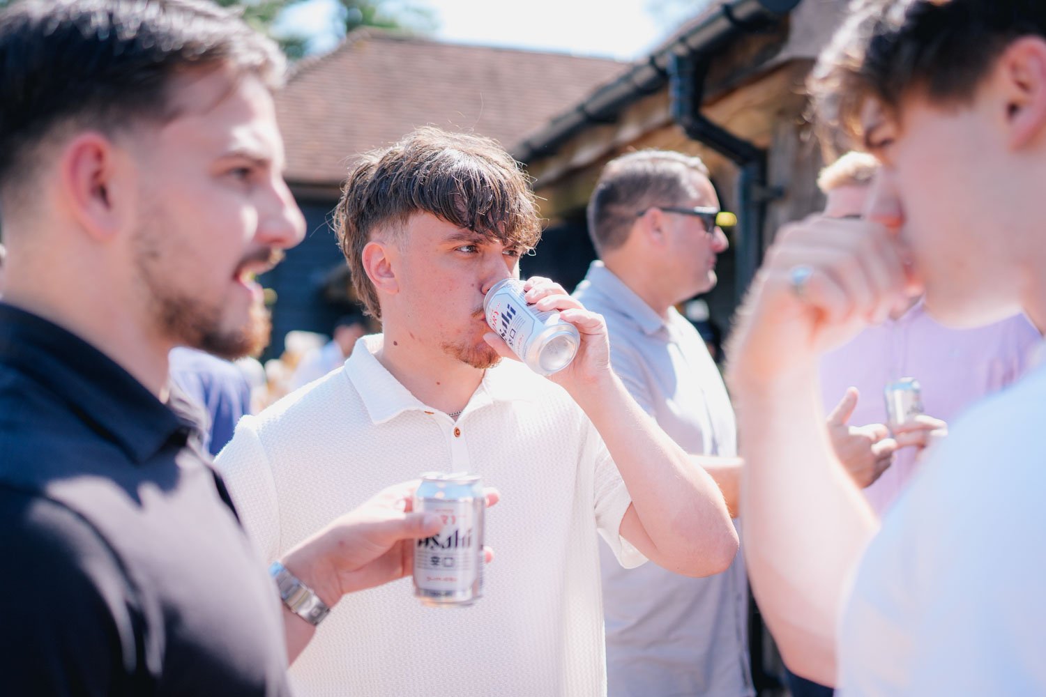 Group of young men outdoors, one drinking a can of Asahi beer.