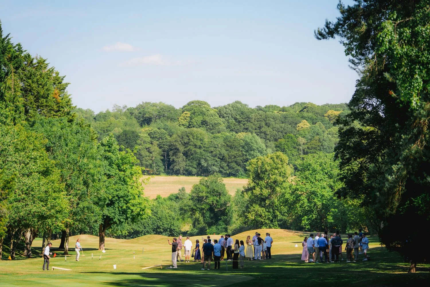Group of people gathered on a golf course surrounded by trees and greenery during daytime.