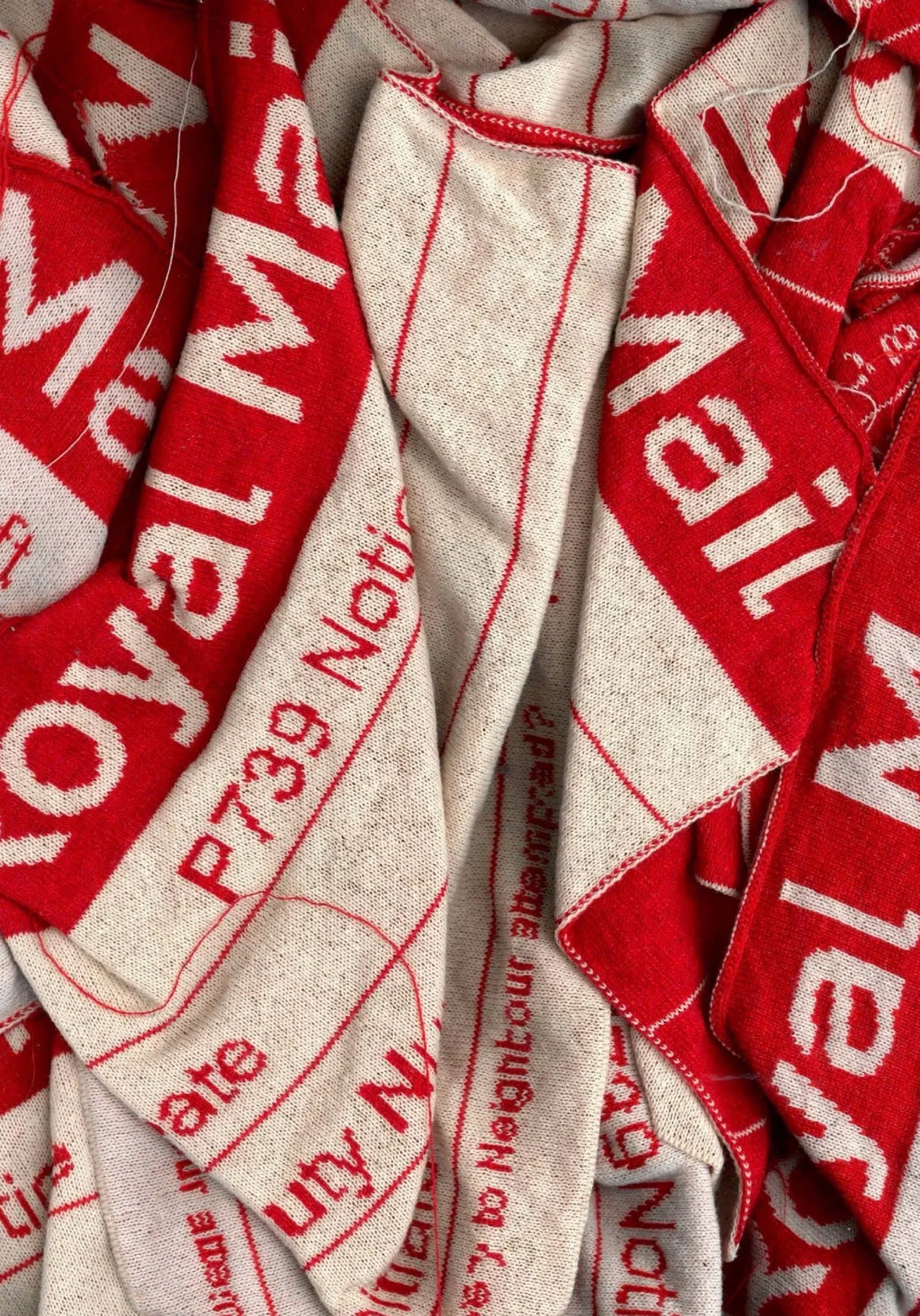 Close-up of crumpled red and white fabric with printed text and lines, resembling a vintage or retro textile or cloth with partial words and phrases.