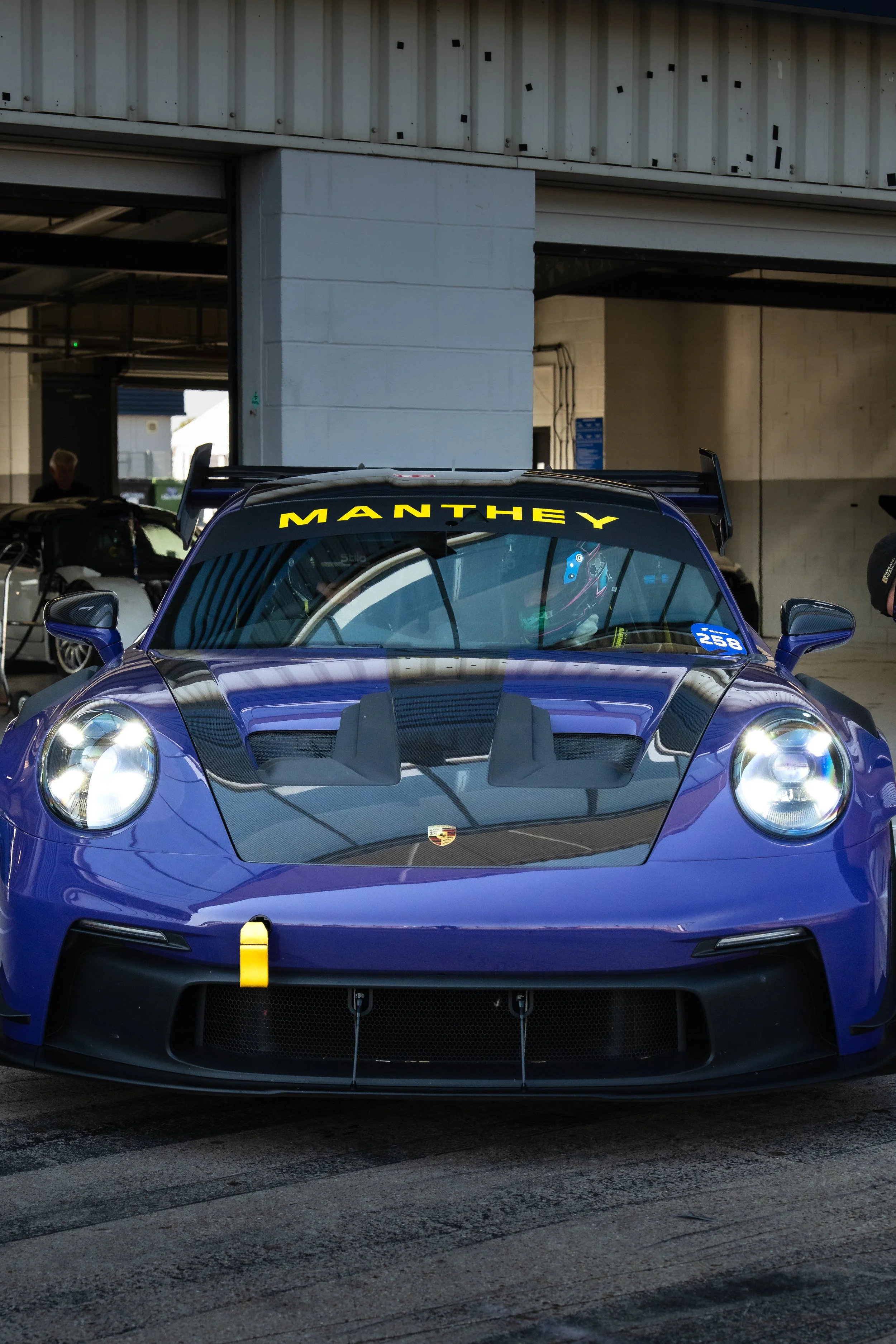 A purple Porsche race car with a black hood and yellow 'MANTHEY' decal on the windshield