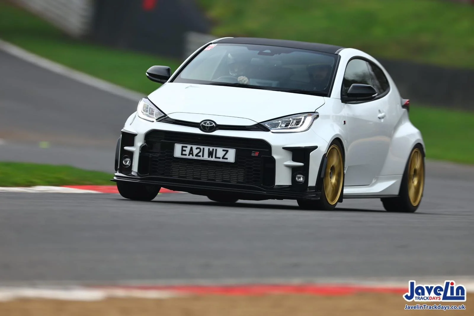 A white Toyota sports car with gold wheels racing on a track.