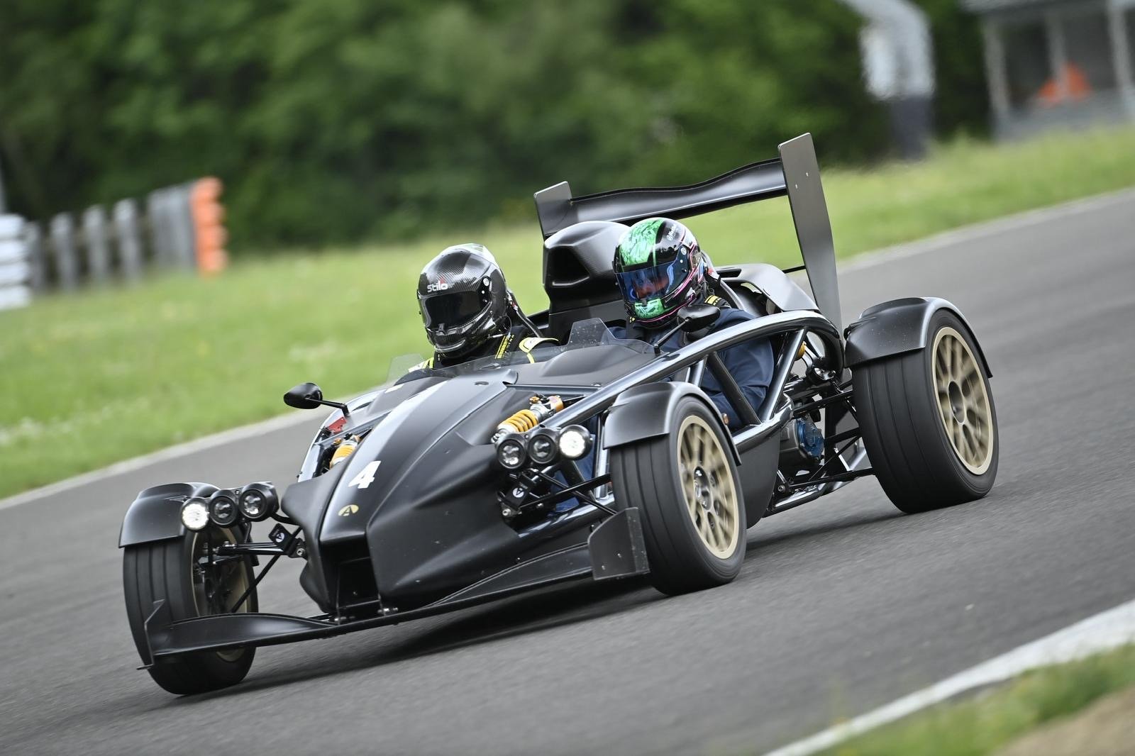 A black race car on a racetrack, driven by two people wearing helmets.