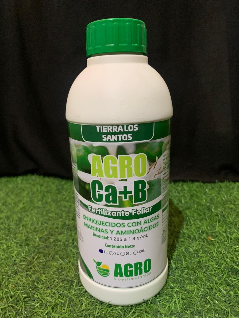 Botella de fertilizante foliar con ingredientes de algas marinas y aminoácidos, marca AGRO, en fondo de césped artificial y fondo negro.