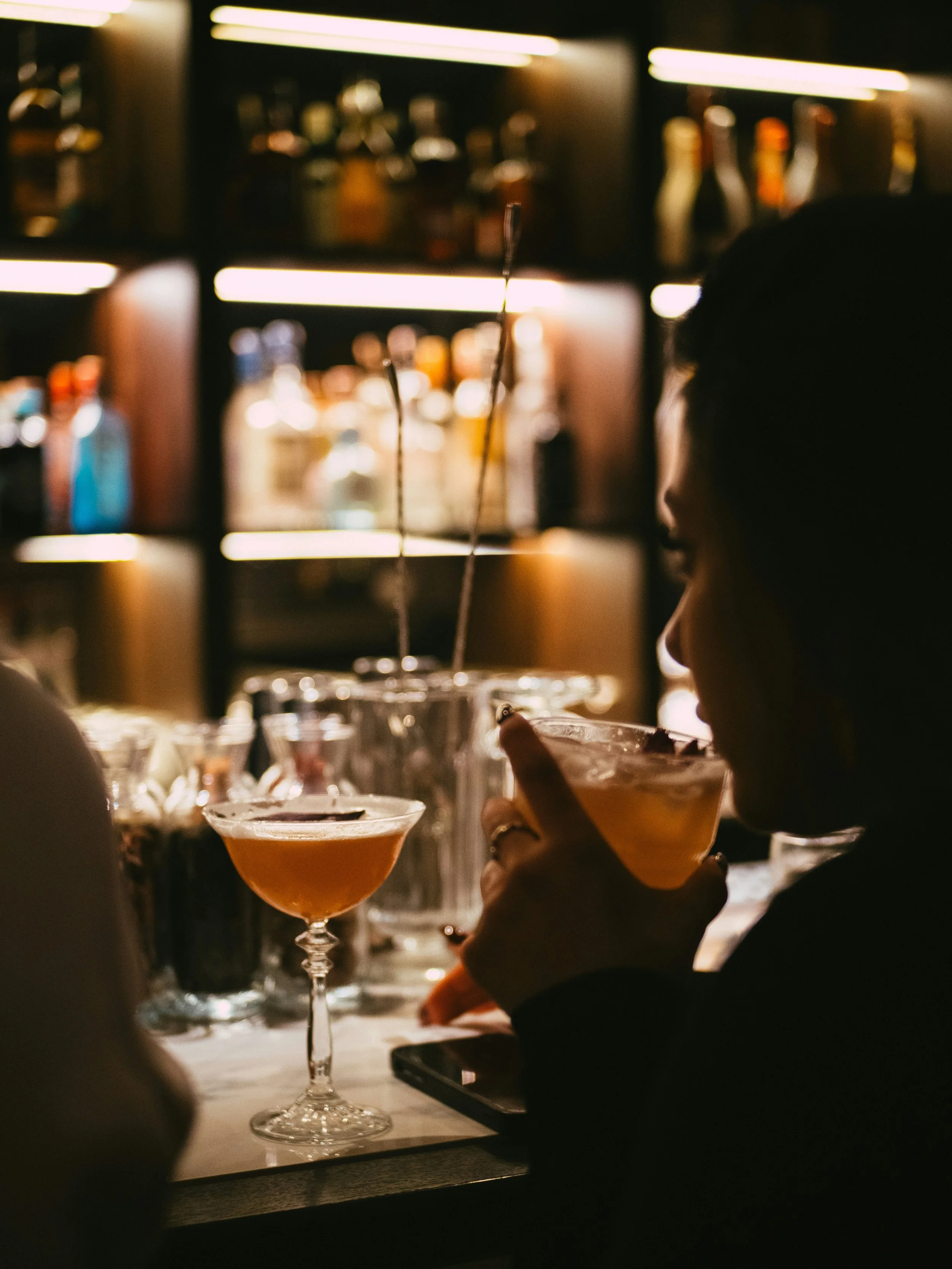 A woman drinking a cocktail at a darkly-lit bar