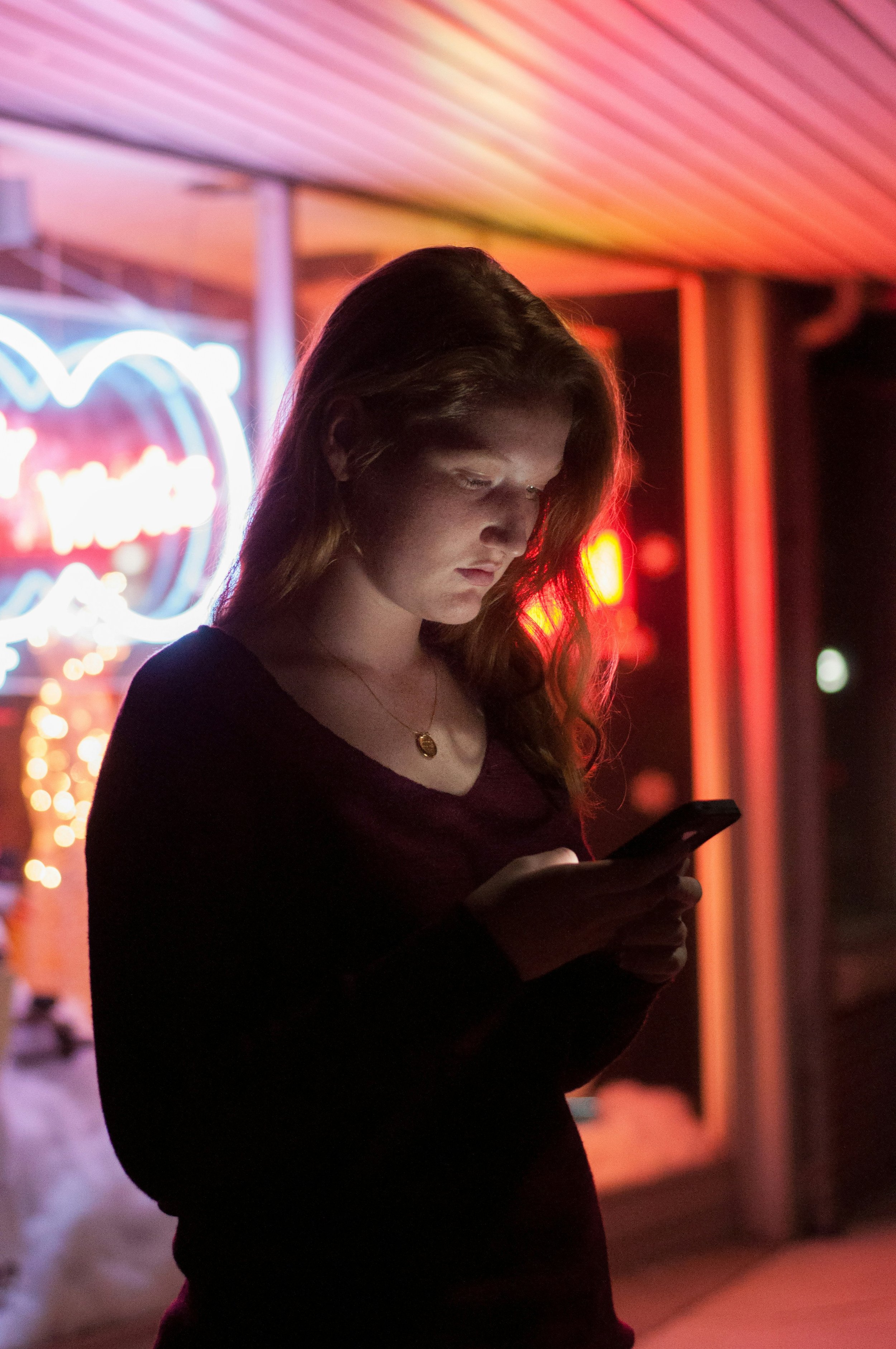A young woman looking at her phone stood outside a venue at night
