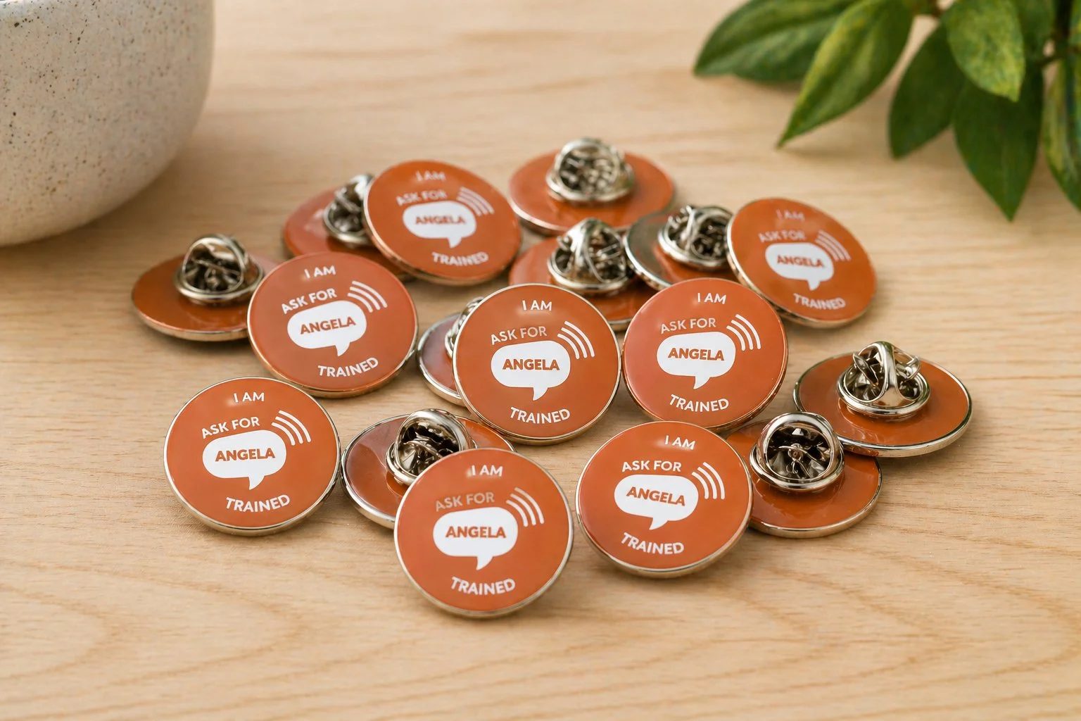 Ask for Angela pile of I am trained pin badges.jpg