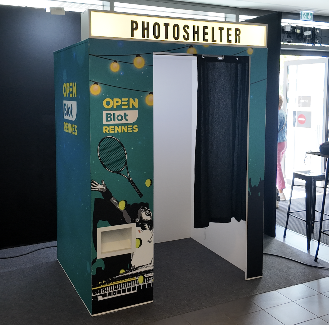 Cabine photo avec une décoration sportive et le texte 'Photoshelter', 'Open Blot Rennes'.