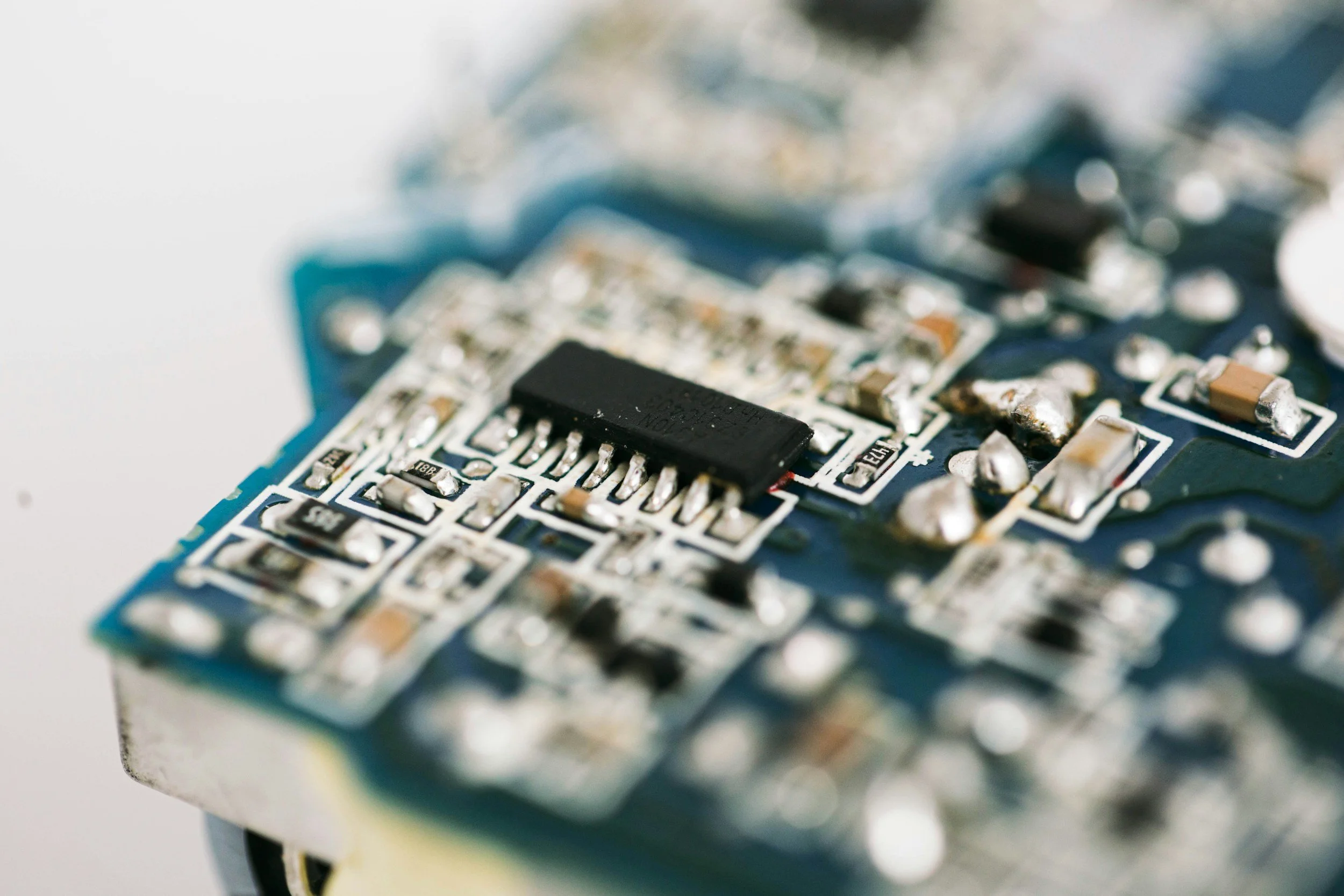 Close-up of a green printed circuit board with a black integrated circuit chip and various small surface-mounted components.