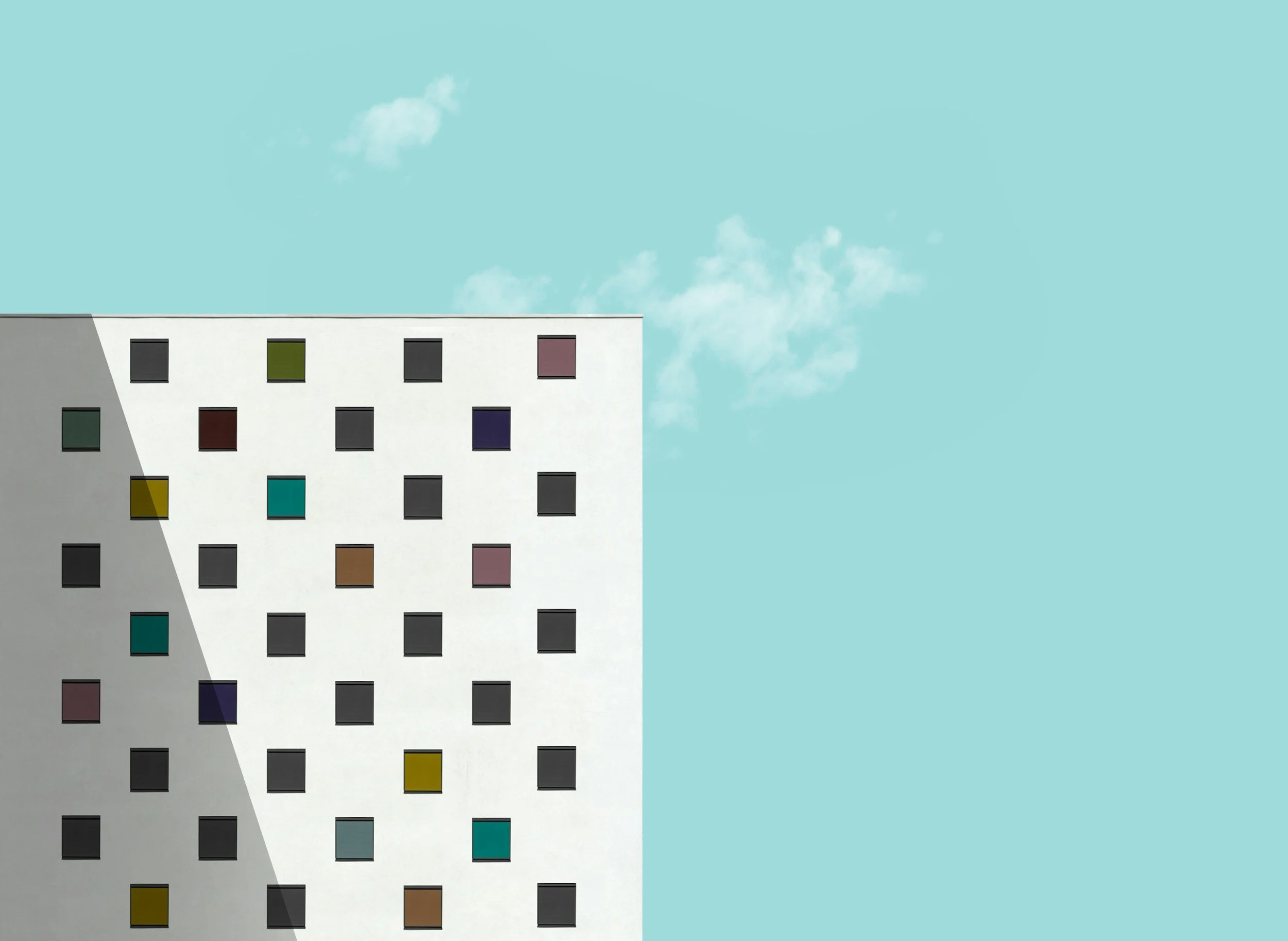 Modern white building with colorful square windows, clear blue sky with a few clouds.