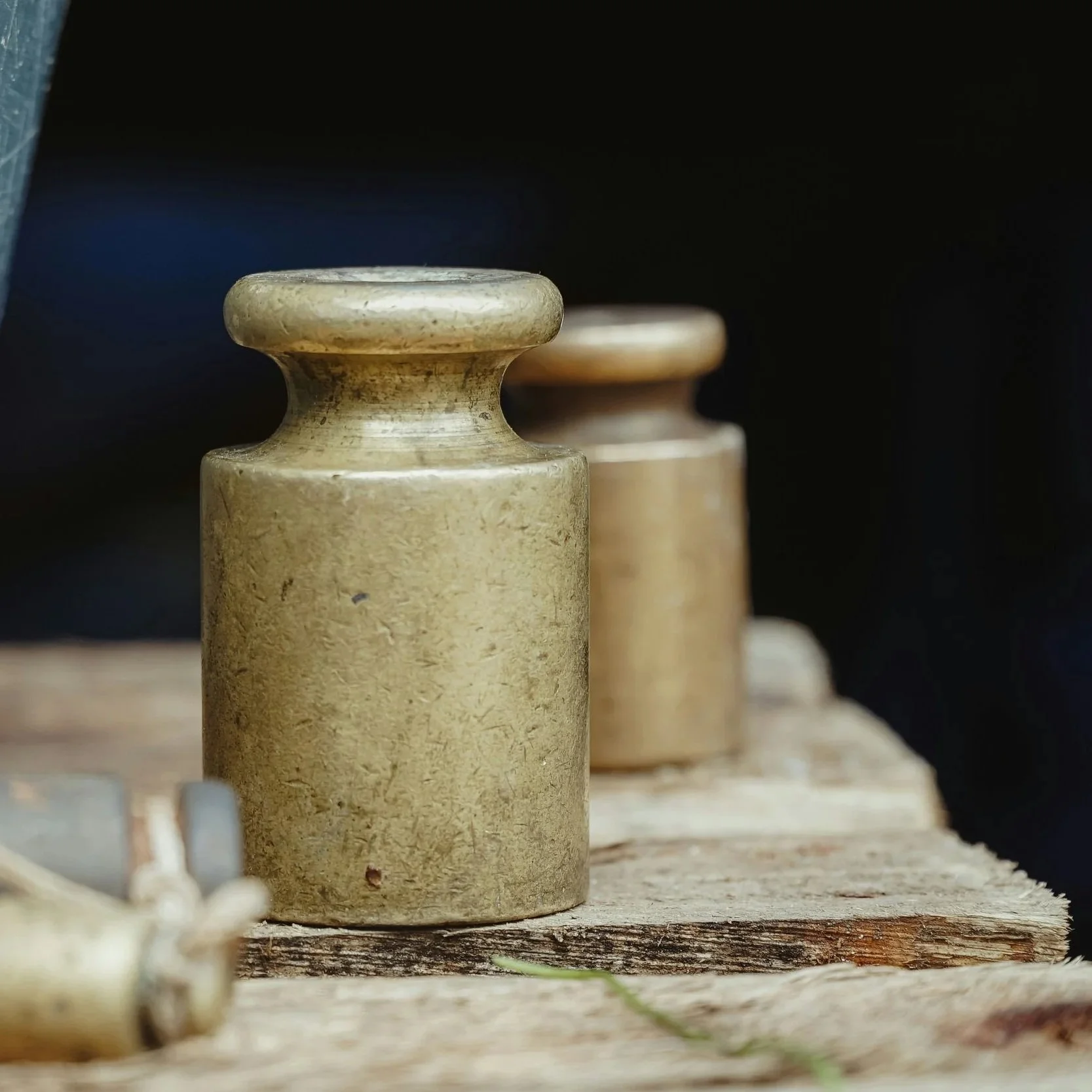 Close-up of two vintage brass weights on a wooden surface with a dark background.