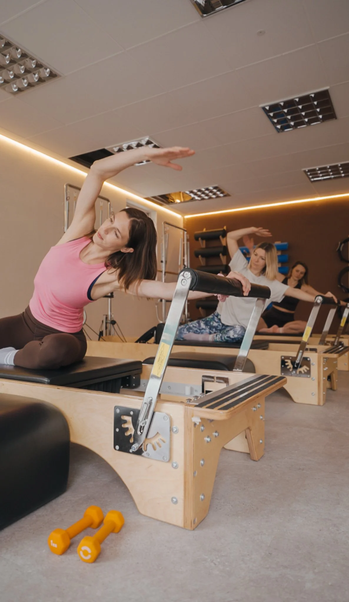 Women participating in a Pilates class on reformer machines in a fitness studio.