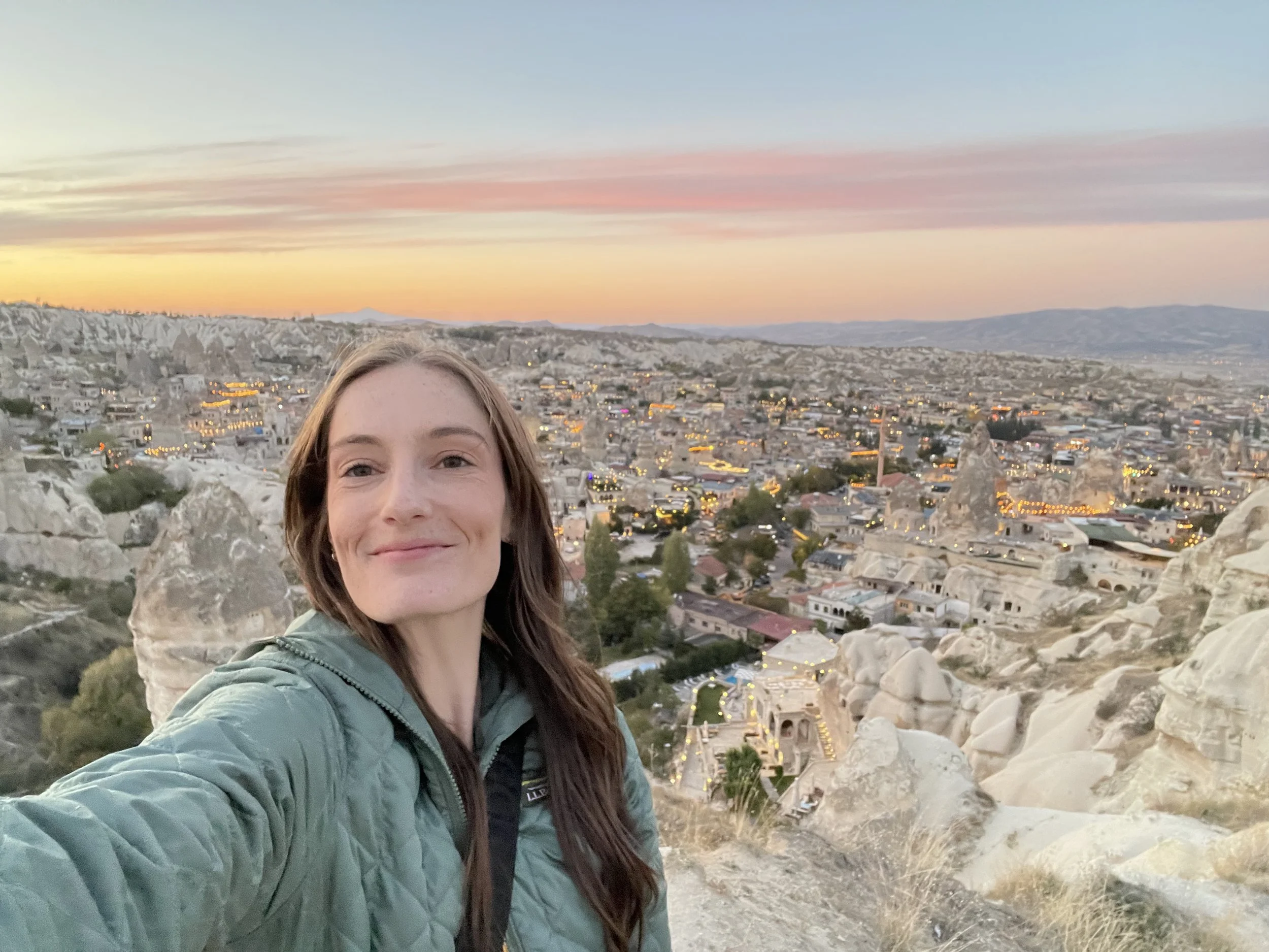 A woman therapist taking a selfie with a cityscape and rocky landscape in the background during sunset.