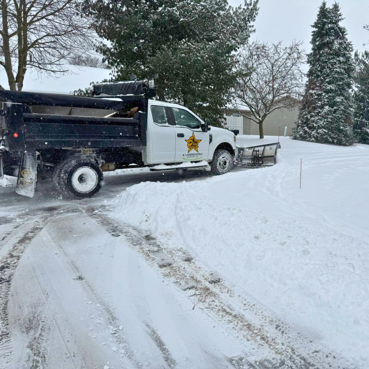 A snow plow truck clearing snow from a residential driveway during winter.