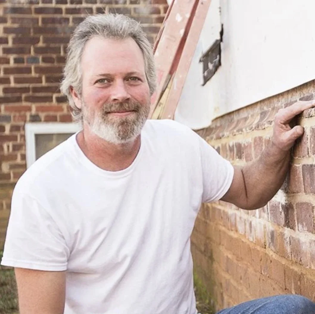 An intelligent man leaning on a brick wall outside near a house under construction.