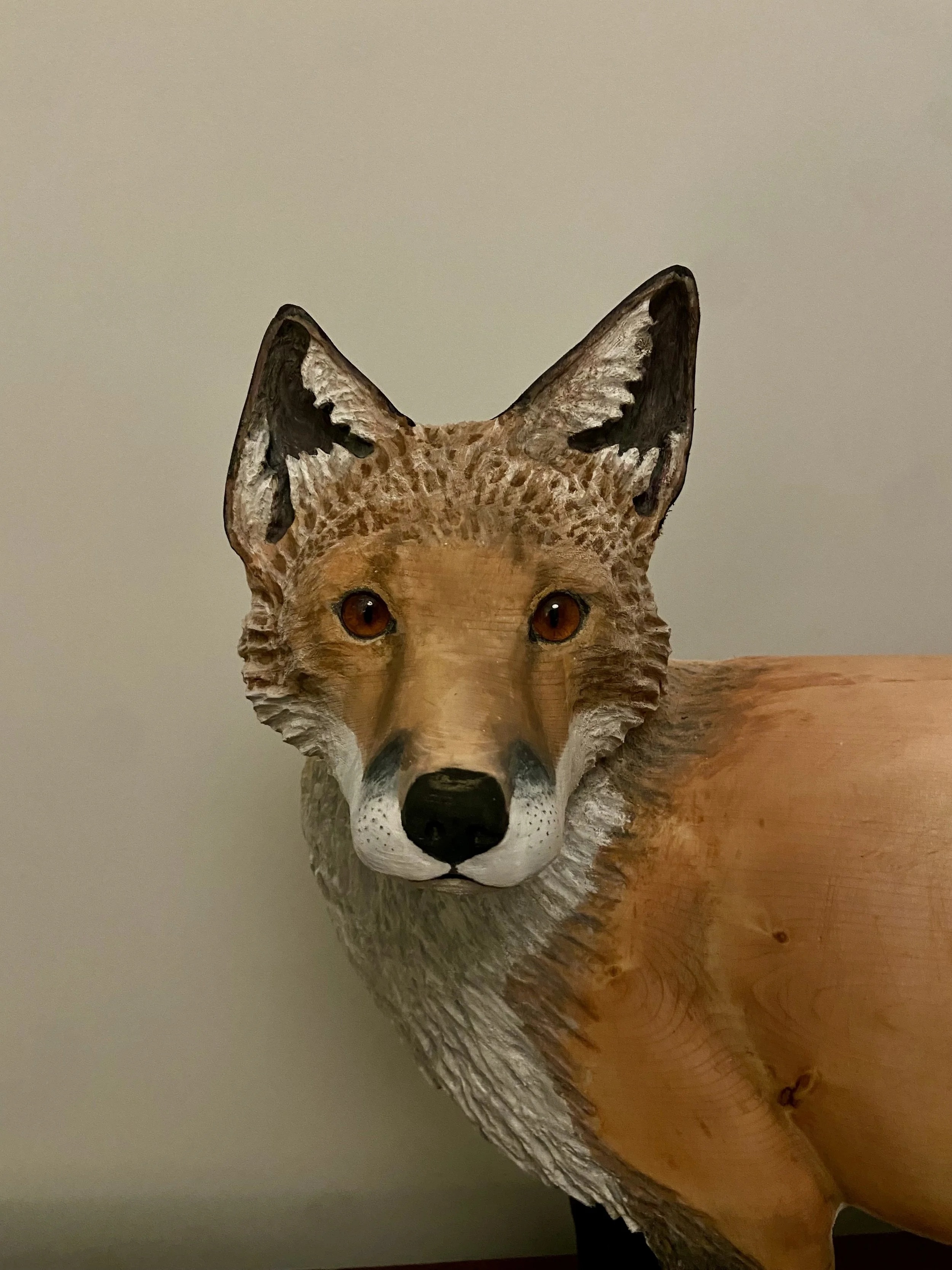 A detailed wooden carving of a fox, showing its face and part of its body, with natural wood grain details and realistic features.