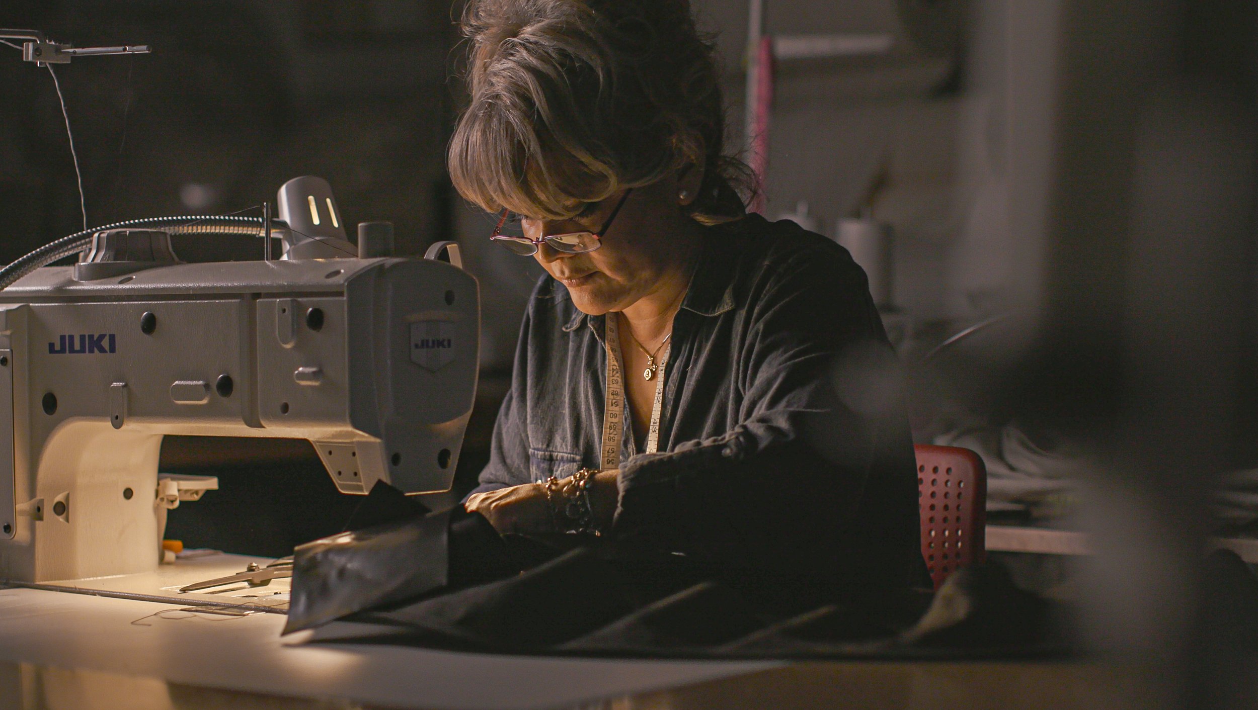 A woman working at a sewing machine in a dimly lit workshop.