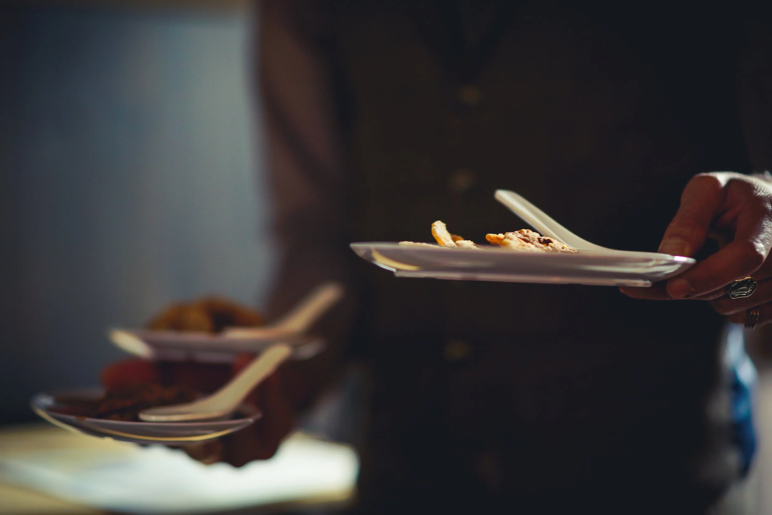 Person holding a white plate with food, with other plates of food on the table.